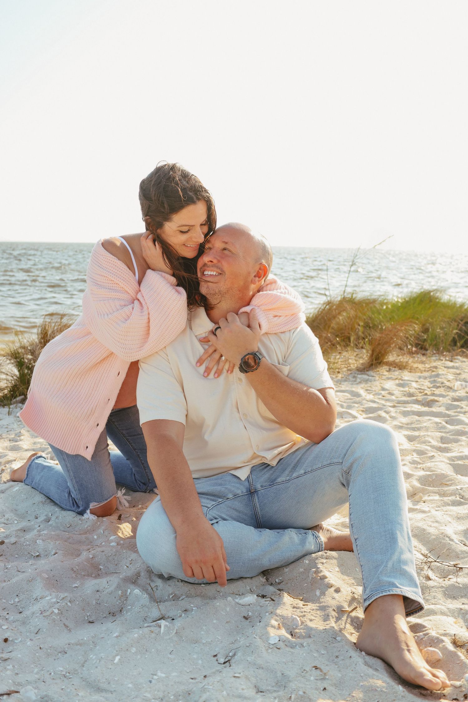 Playful couple lounges on white sand beach during a sunny afternoon photoshoot.