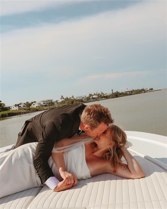 Romantic couple shares intimate moments on cushioned boat deck with coastal view.