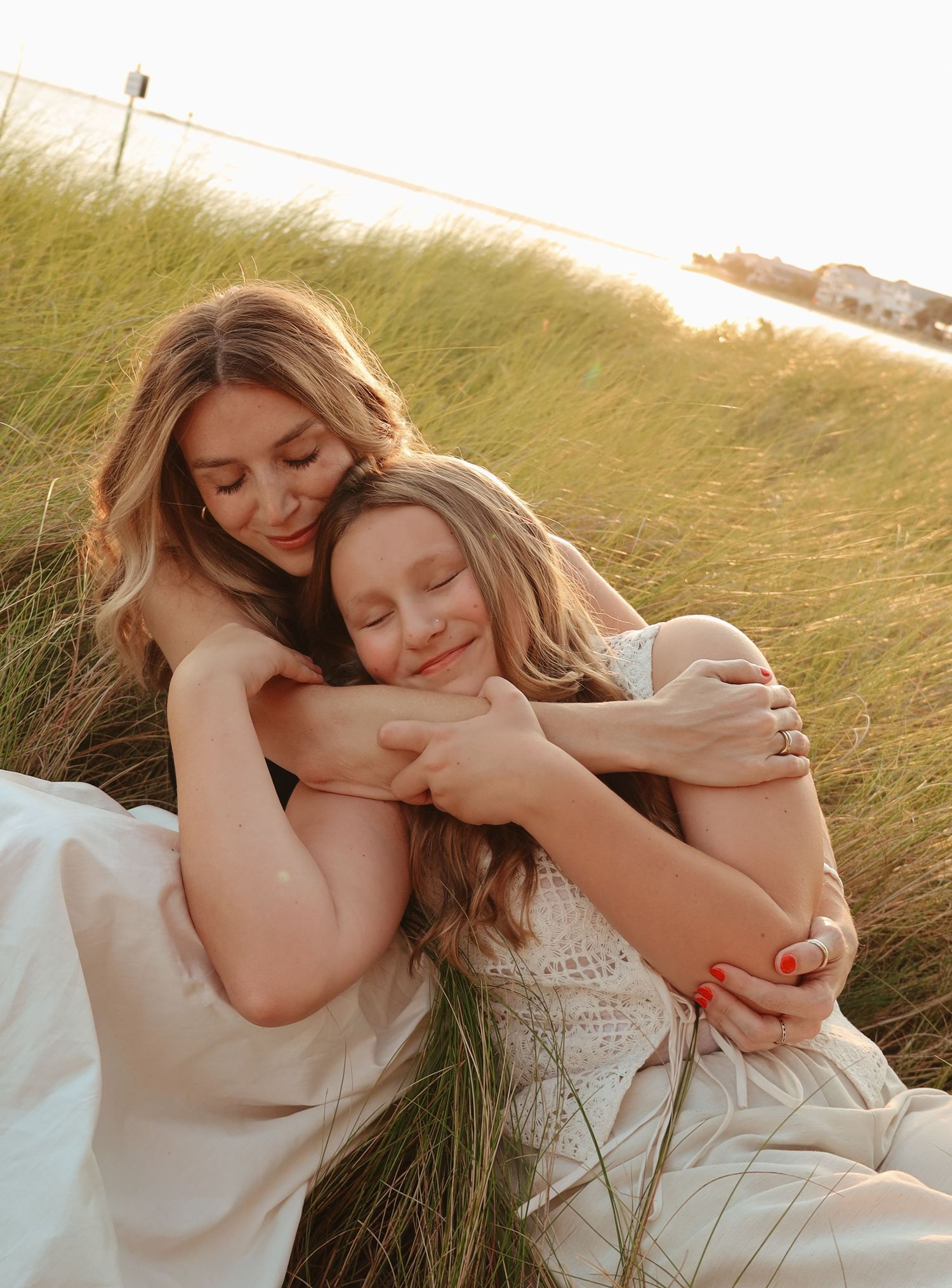 A couple in white dresses share intimate moments together in a grassy field during golden hour.