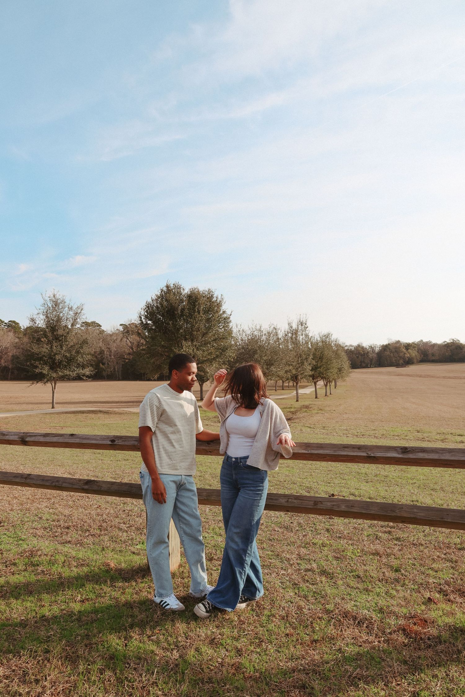 Two people walk together across a grassy field on a sunny autumn day with trees in the background.