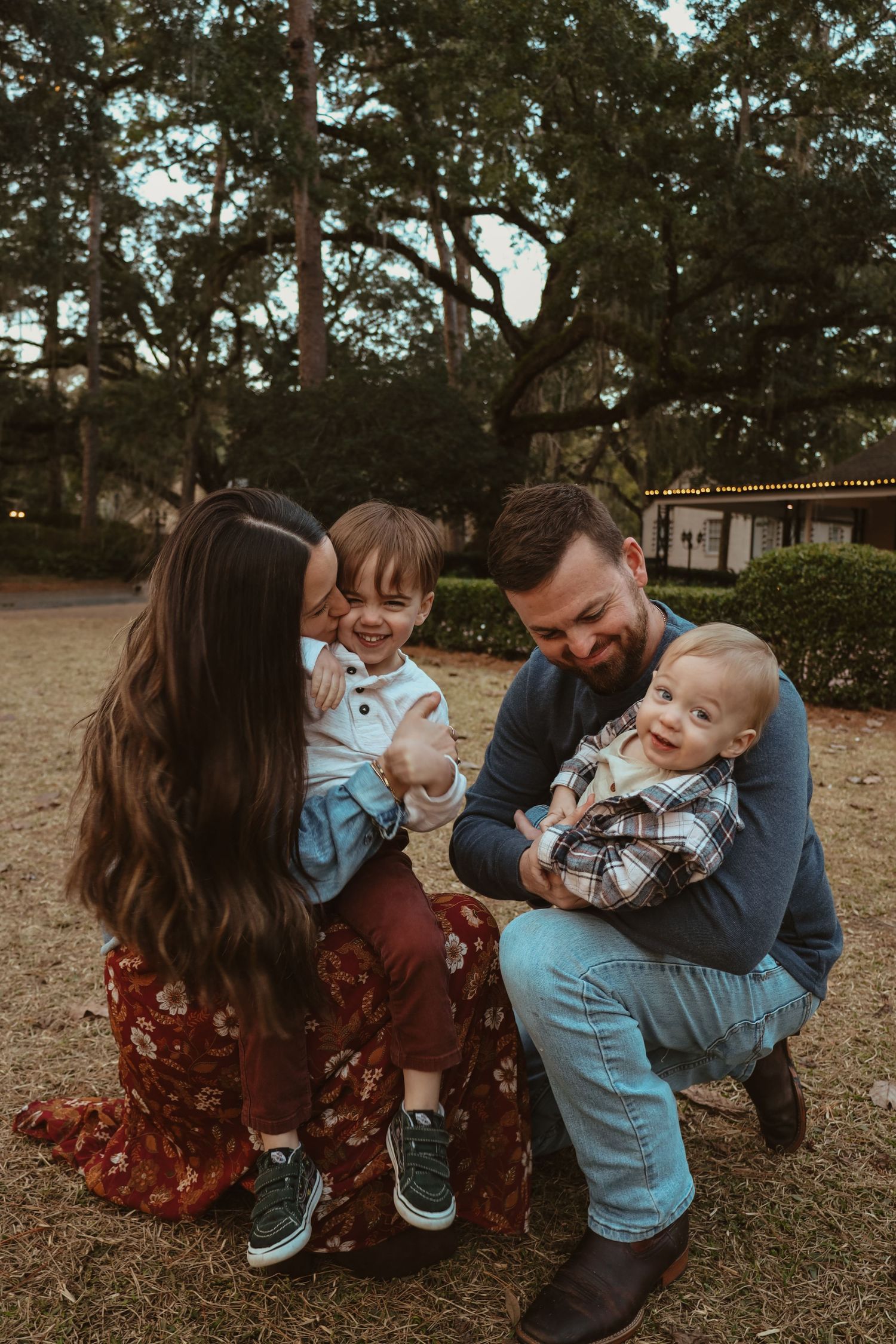A loving family sits together on autumn grass sharing playful moments with their baby in a park setting.