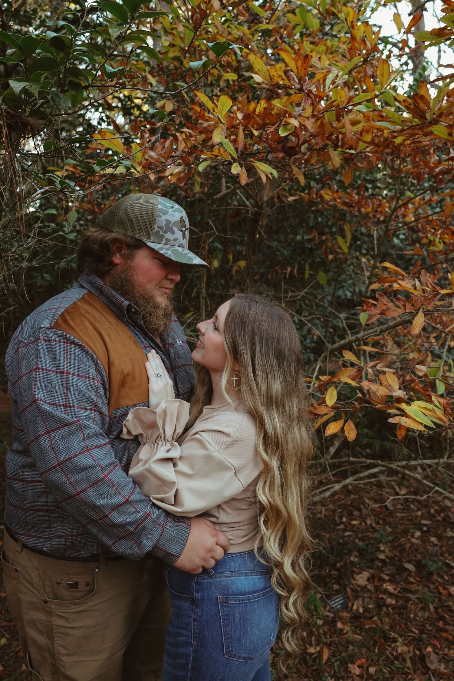 Romantic autumn engagement photos showing a couple embracing among colorful fall foliage in a natural setting.