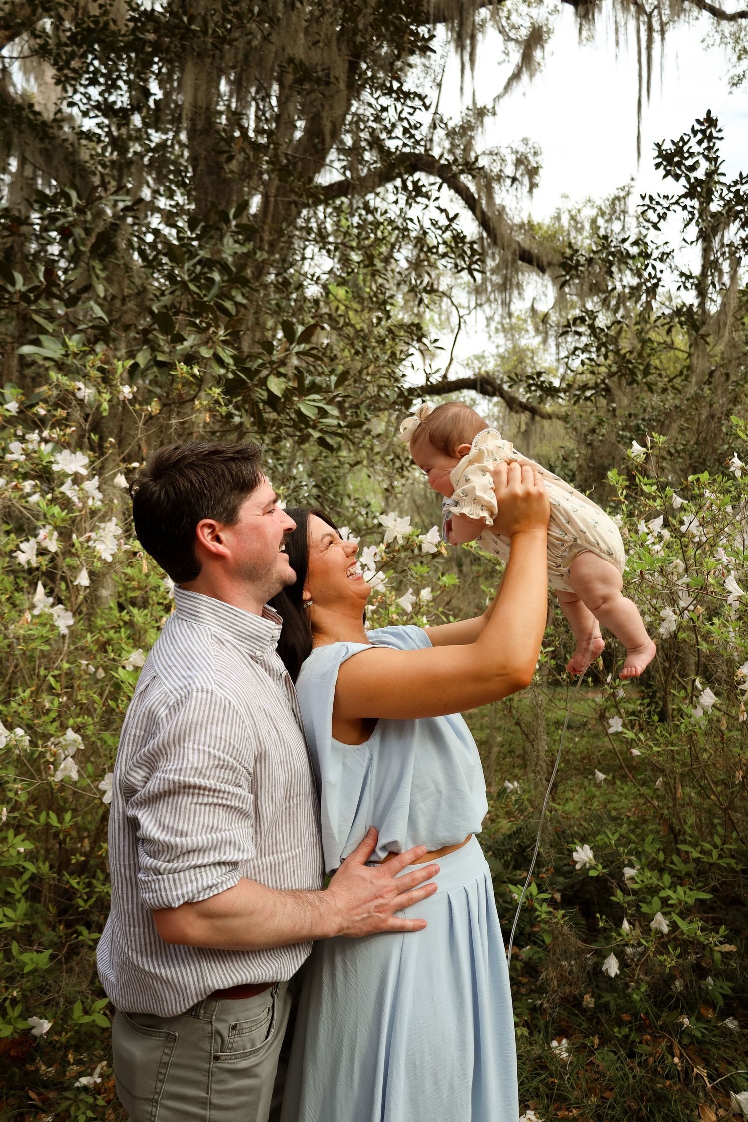 A family shares a joyful moment together outdoors among Spanish moss draped trees and flowering bushes.