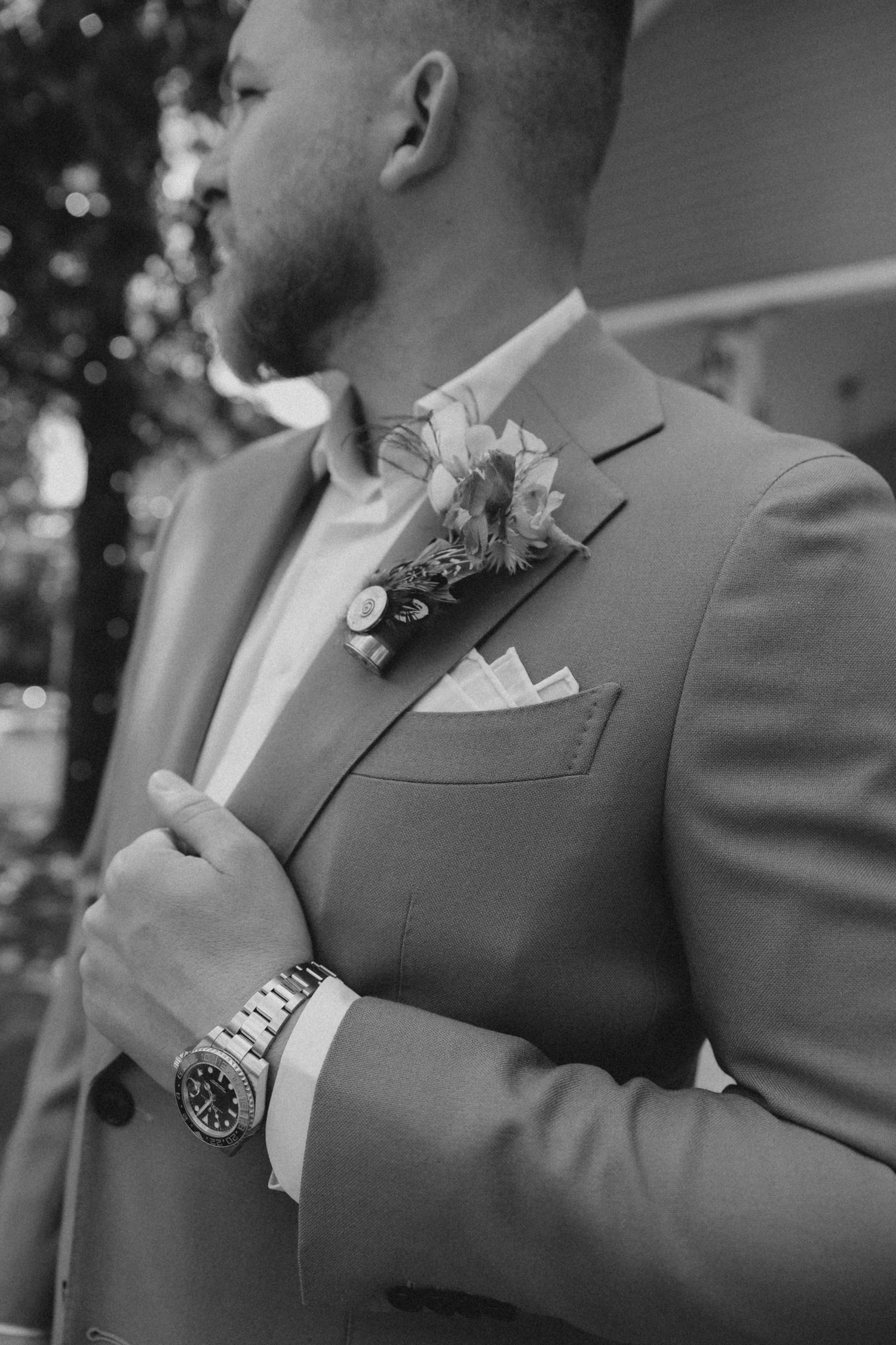 Black and white photo of a groom in a suit with boutonniere and pocket square, adjusting his jacket on his wedding day.