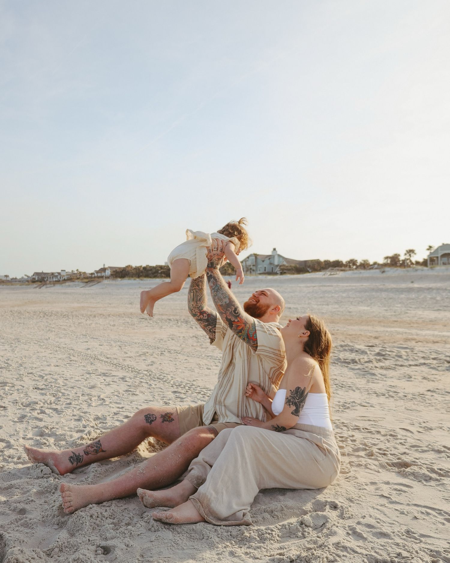 Couple in light-colored attire shares playful moments on sandy beach at dusk.