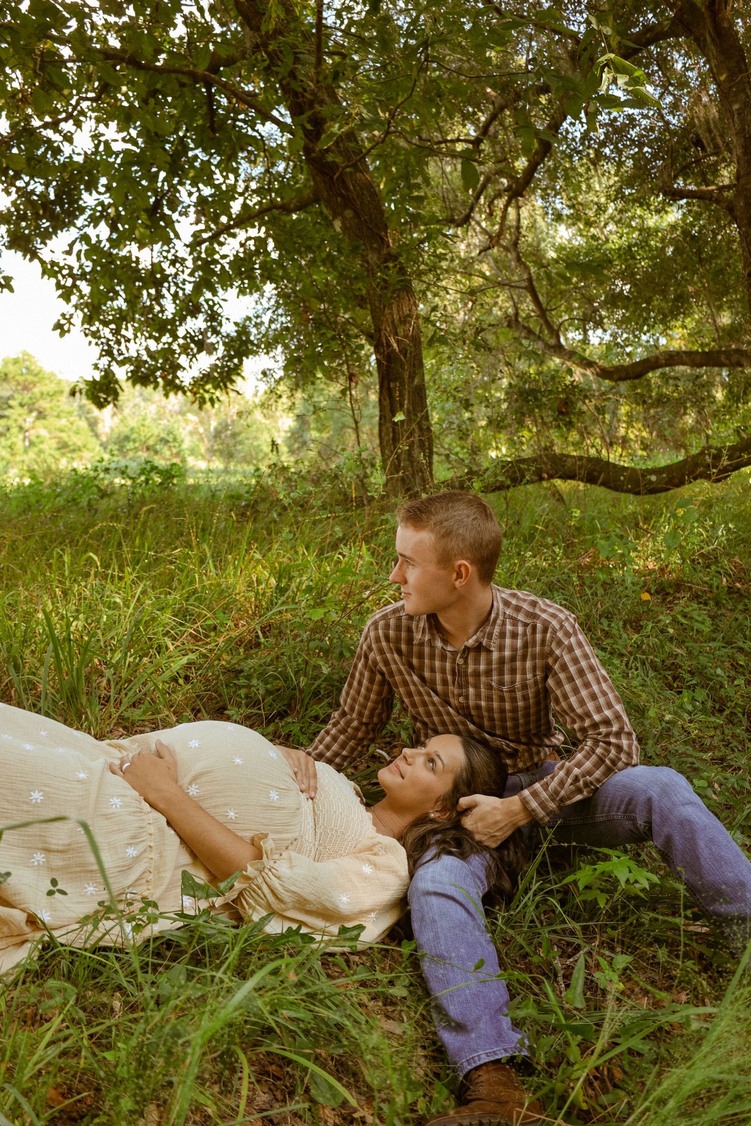 A couple sharing intimate moments while resting in tall grass during a photo session.