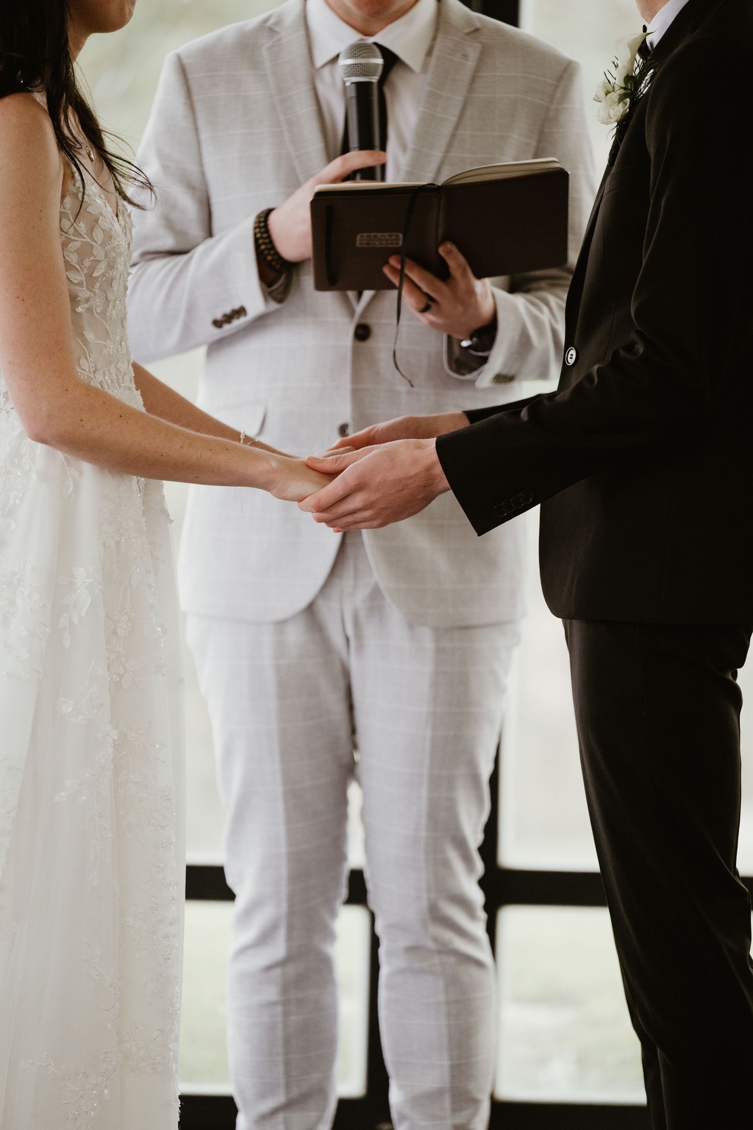 Wedding ceremony officiant holding a book while bride and groom clasp hands.