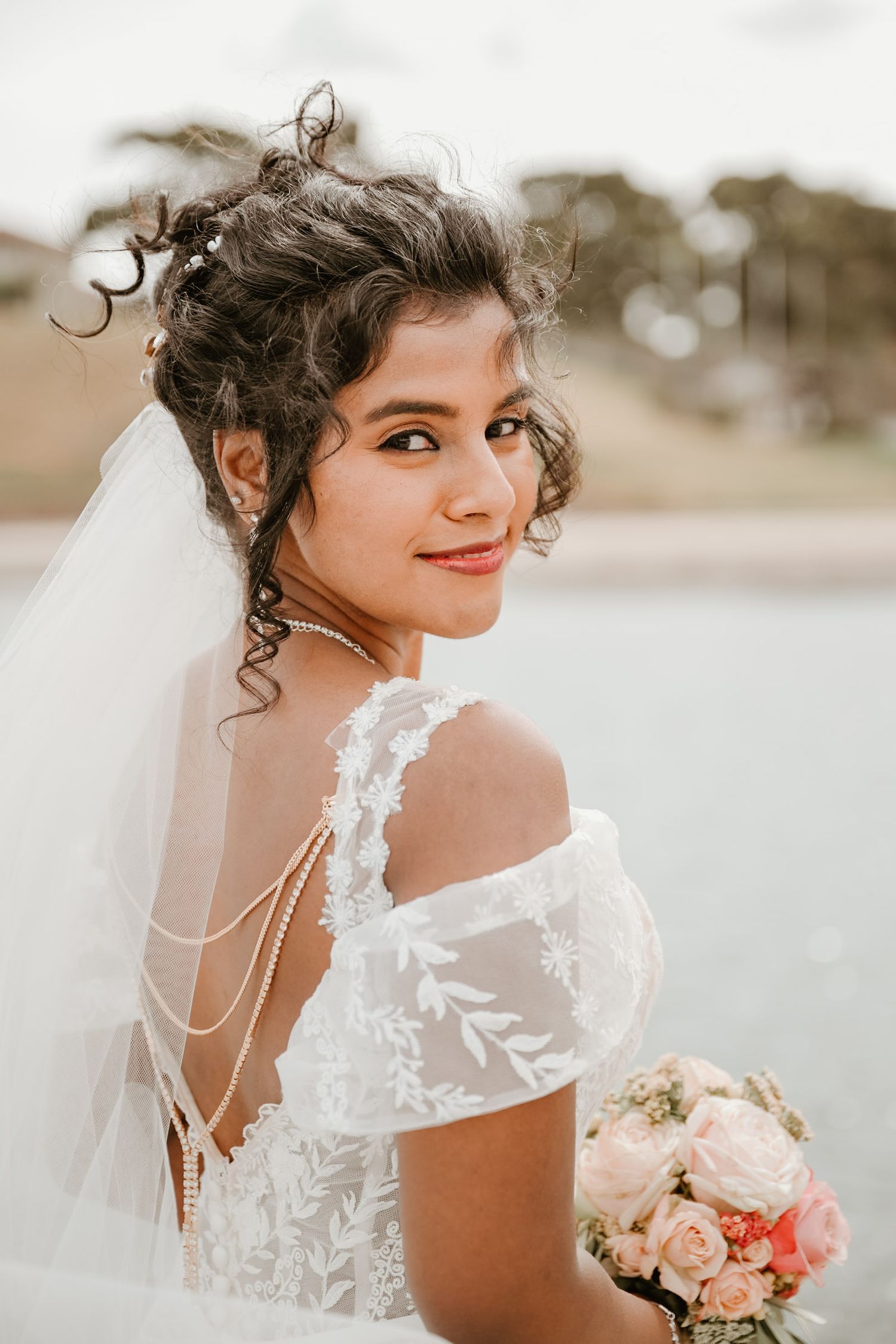 Close up portrait of bride in lace dress with bouquet against soft natural background.
