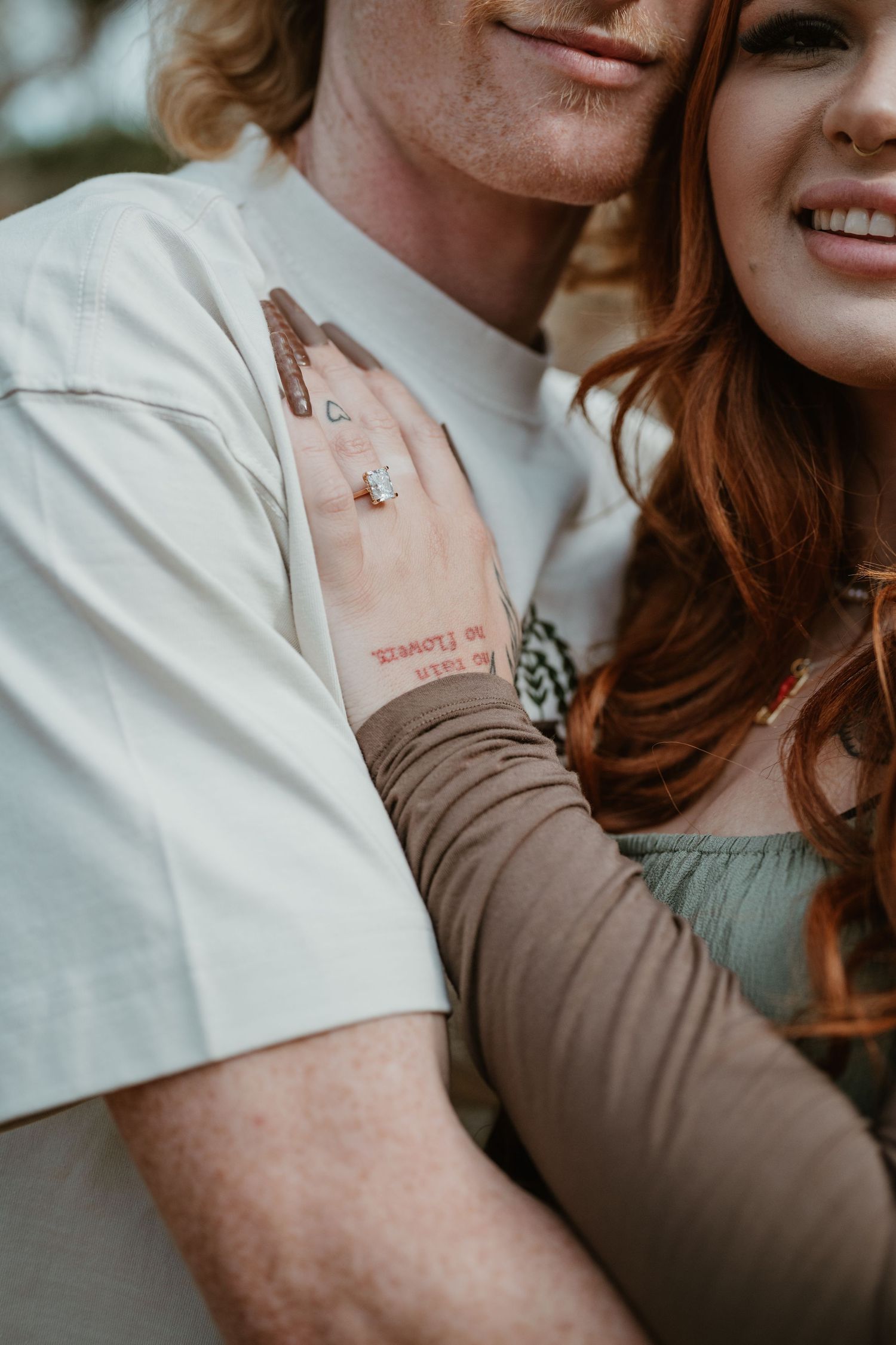 A close-up shot showing tattoos and intertwined hands against neutral clothing backgrounds.