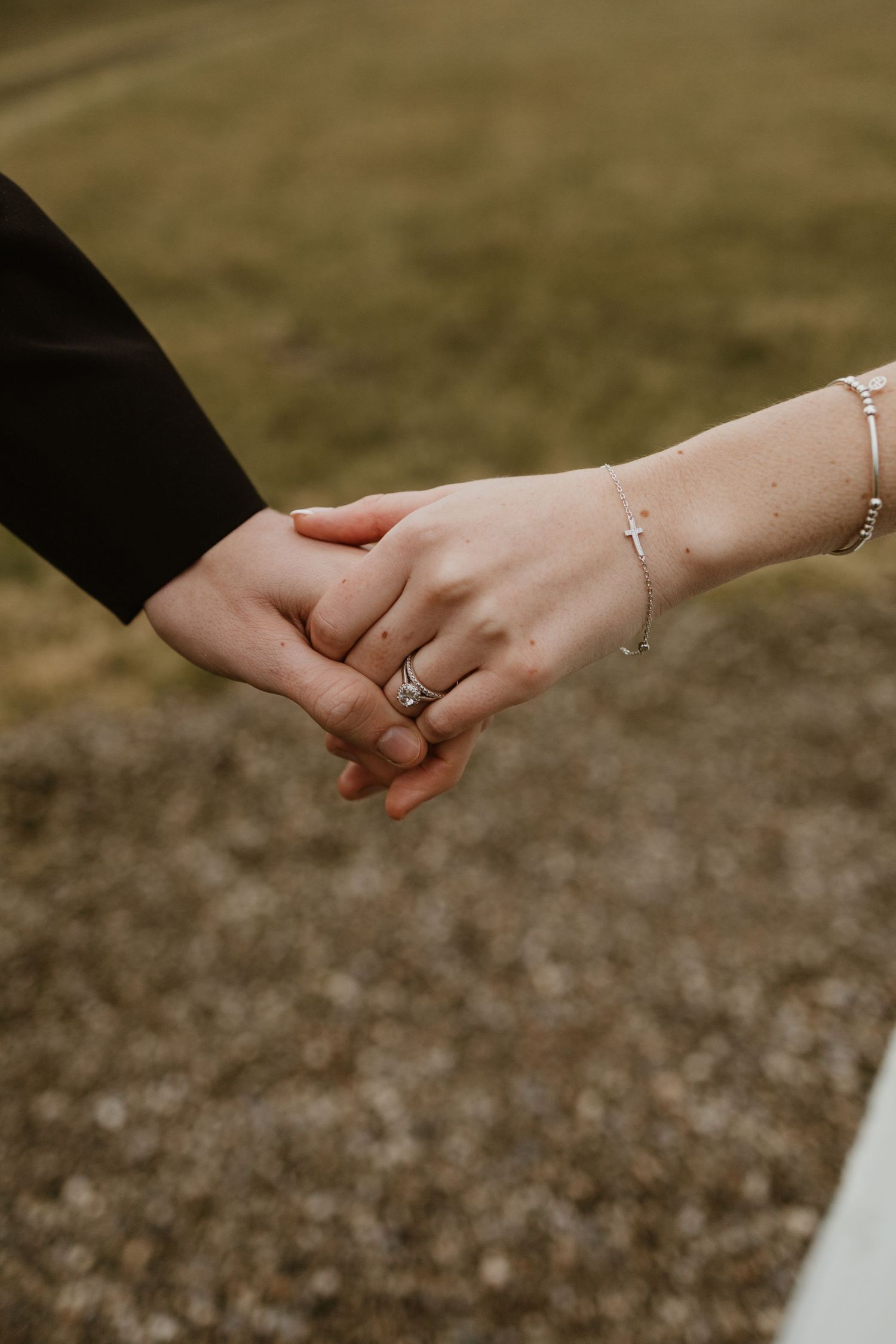 Two hands wearing wedding rings reach toward each other against a natural outdoor background.