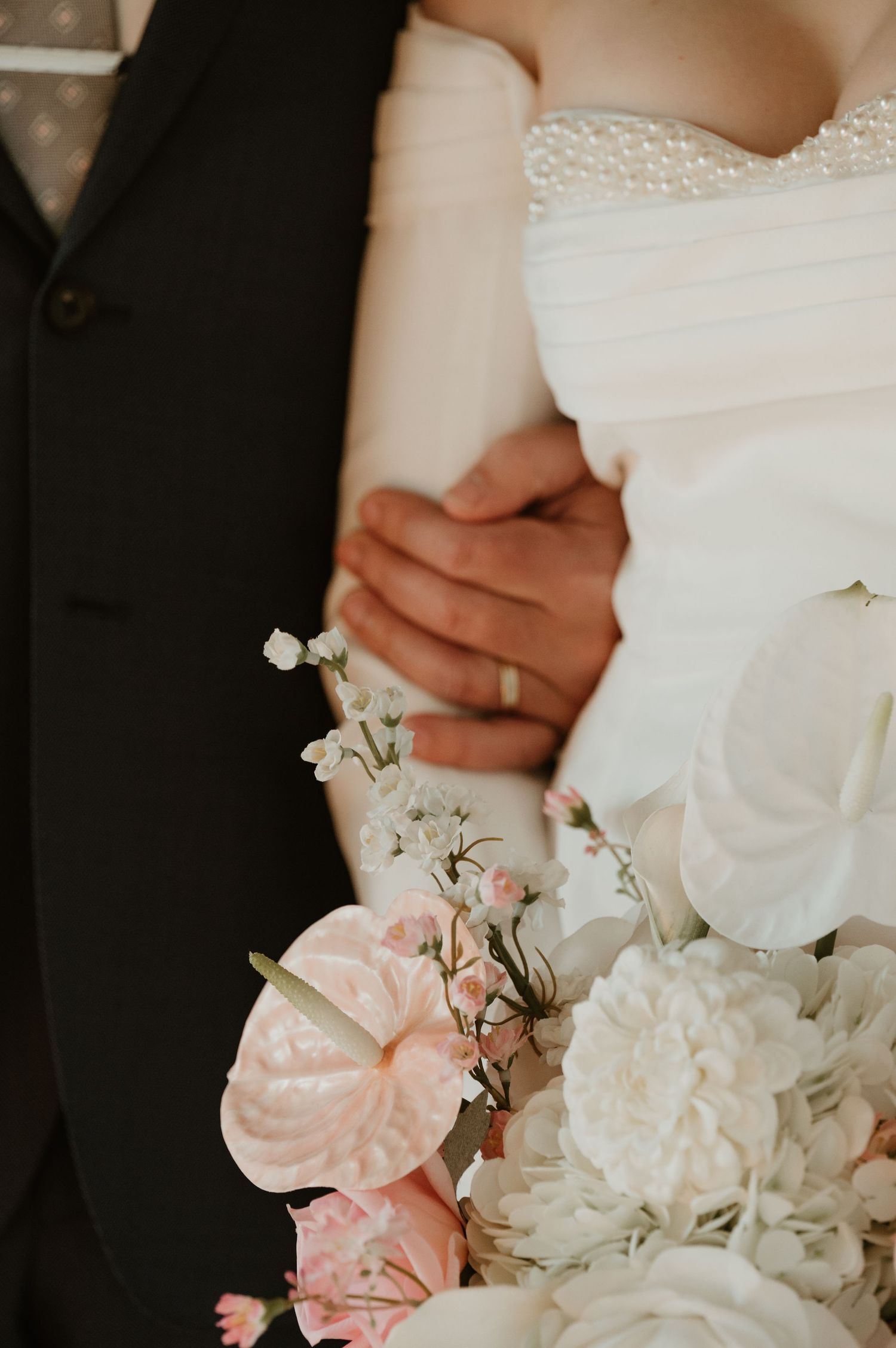Close-up of bride and groom embracing with pink and white wedding bouquet featuring peonies and baby's breath.