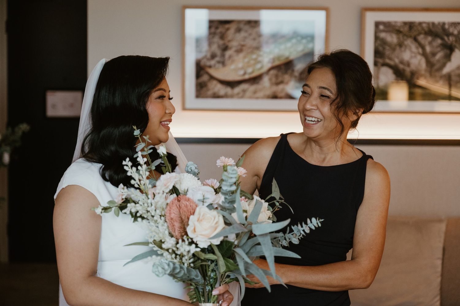 Wedding party members in black dresses hold white floral bouquets while sharing joyful moments during a celebration.