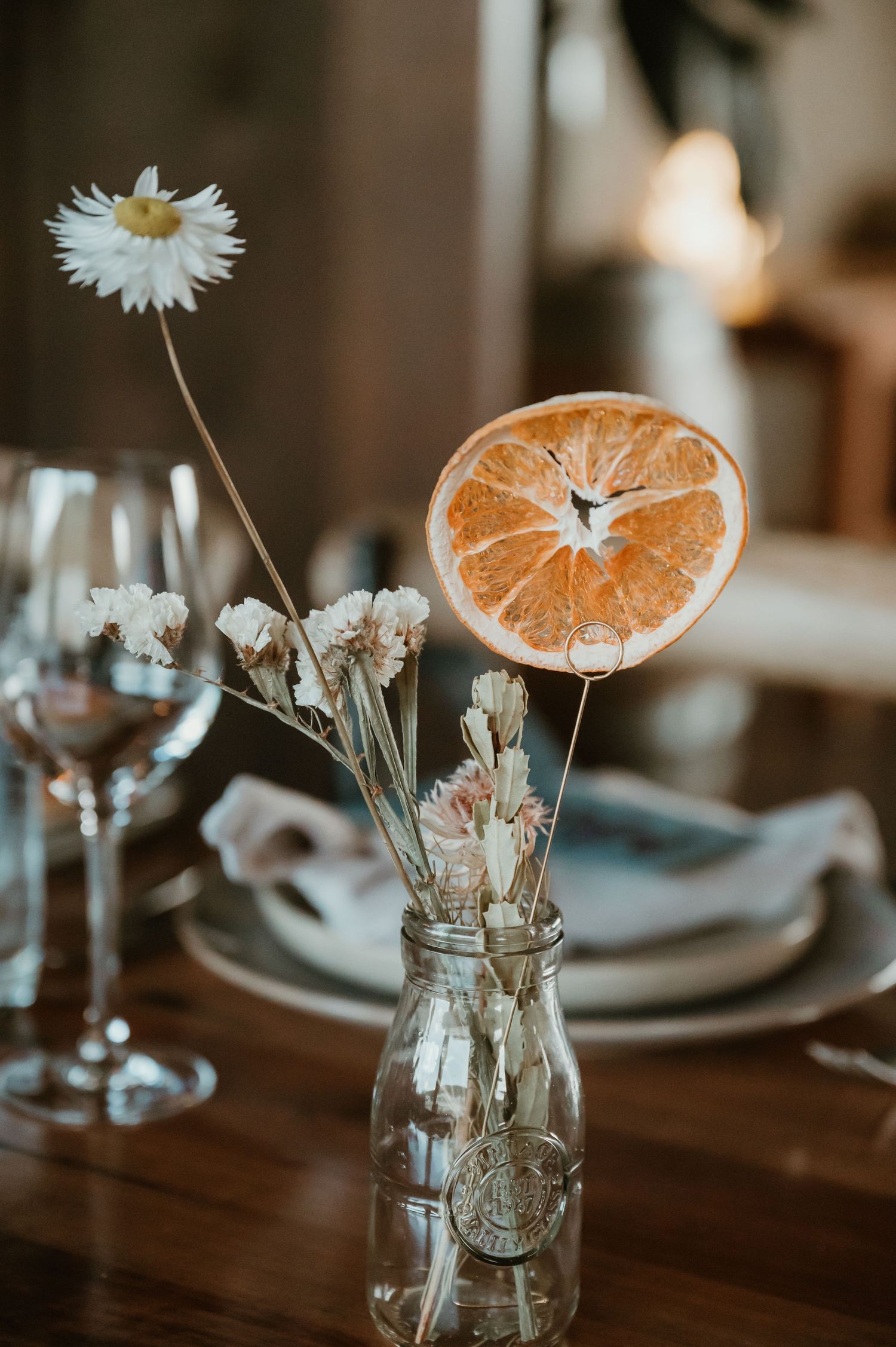 Rustic wedding table decor with dried orange slices and white flowers in mason jar vases.