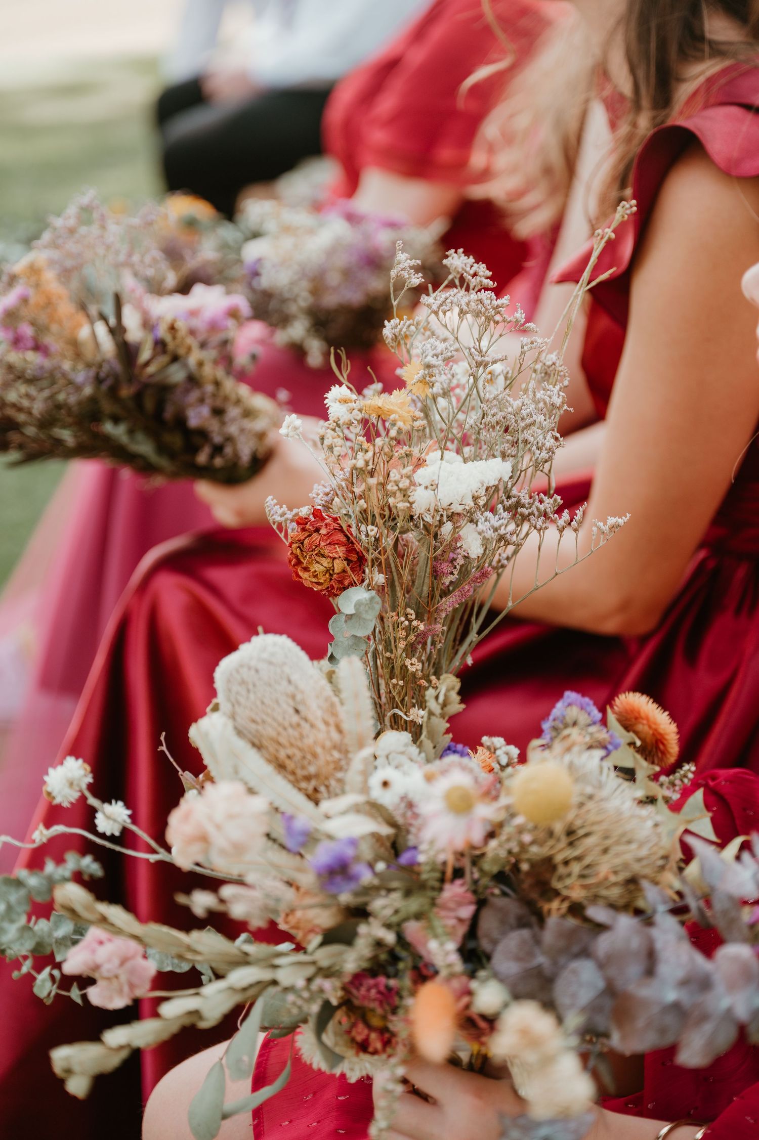 Dried flower bouquets with soft purple and pink blooms rest on a red fabric.