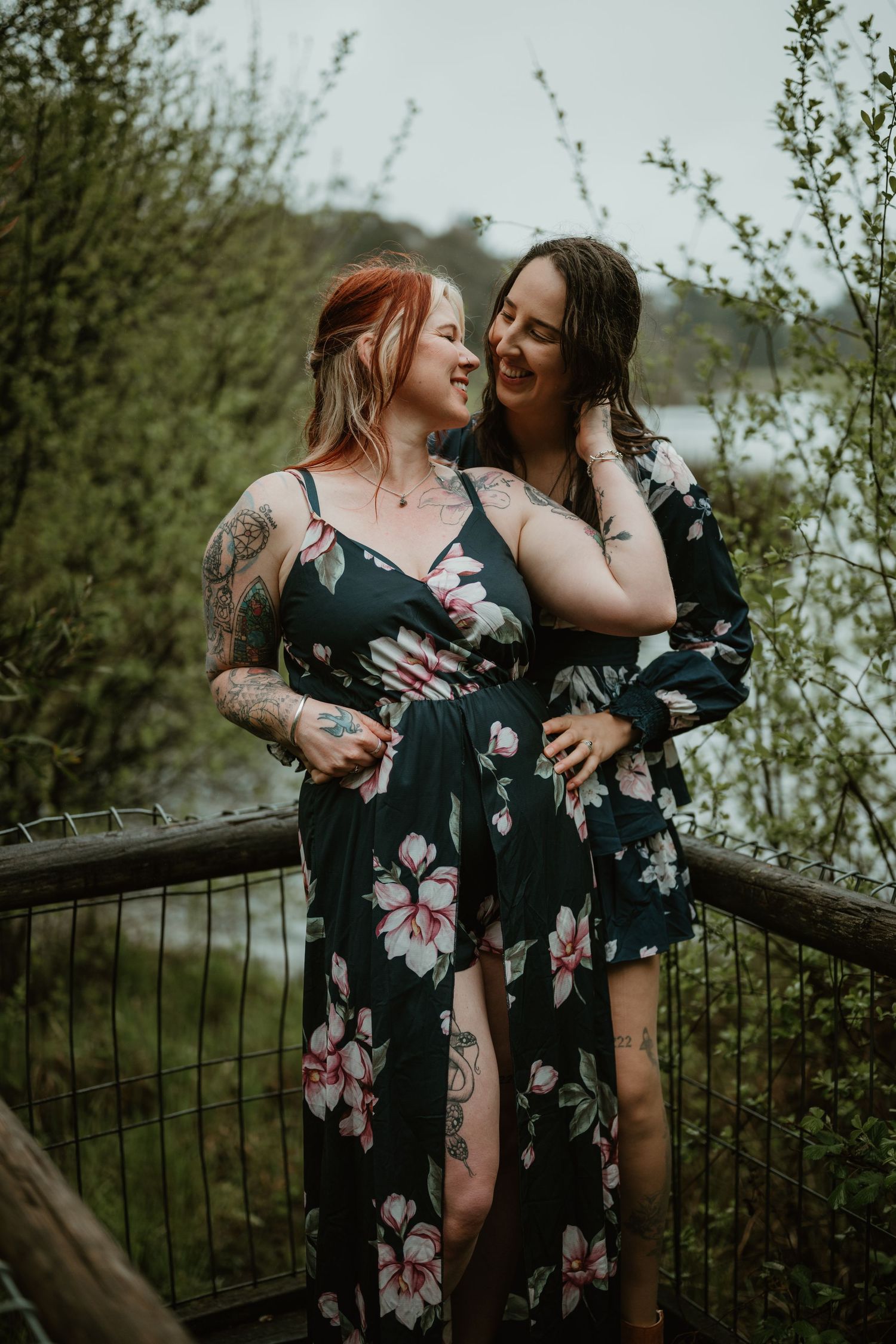 Two people in navy floral dresses laughing together on outdoor deck.