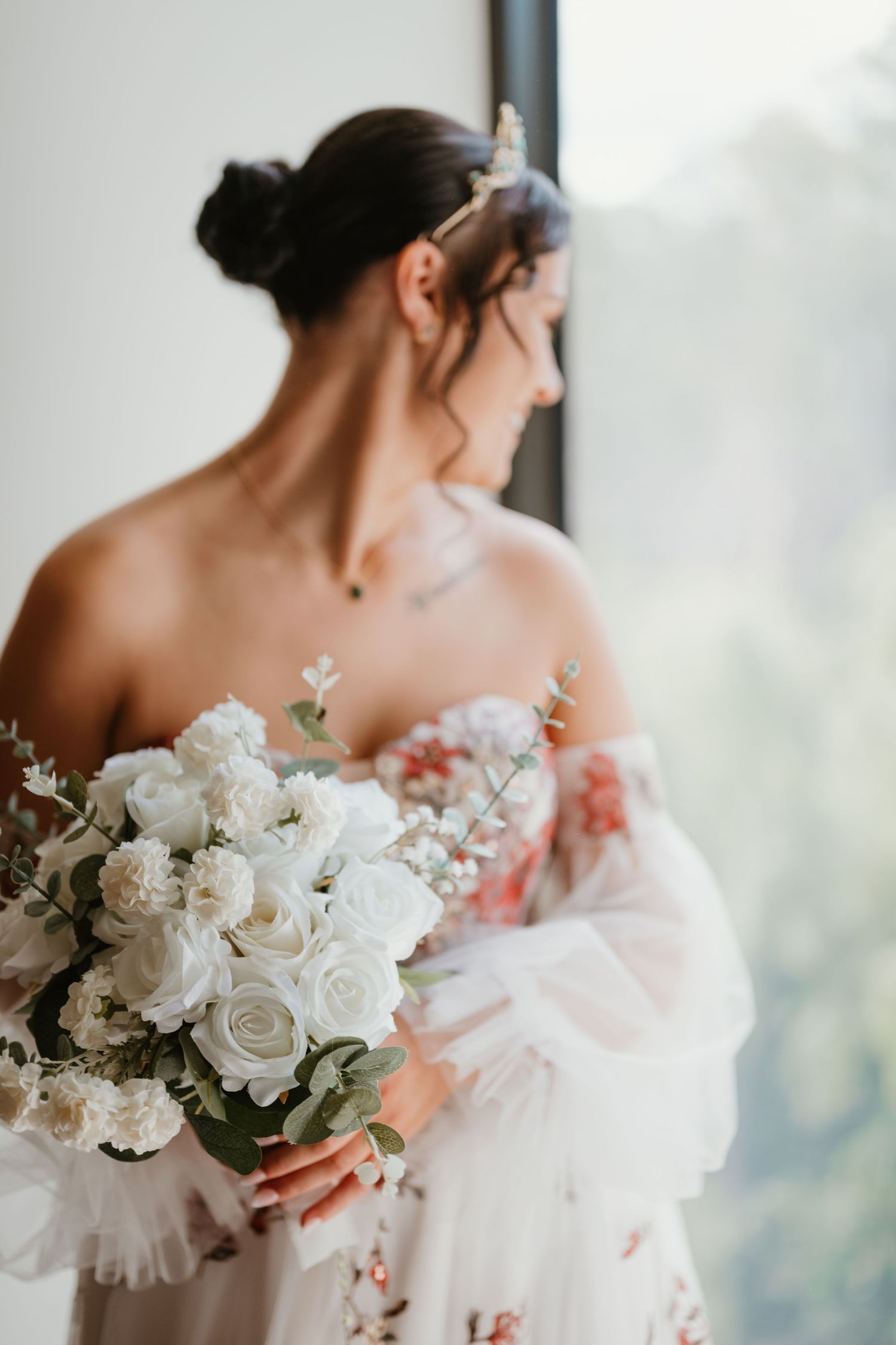 Bride holding white rose bouquet in an elegant off-shoulder floral gown.