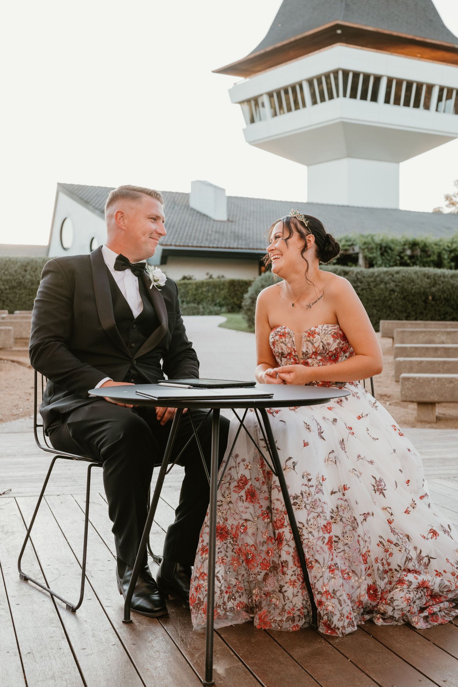 A couple shares a moment at outdoor cafe tables during their wedding day.