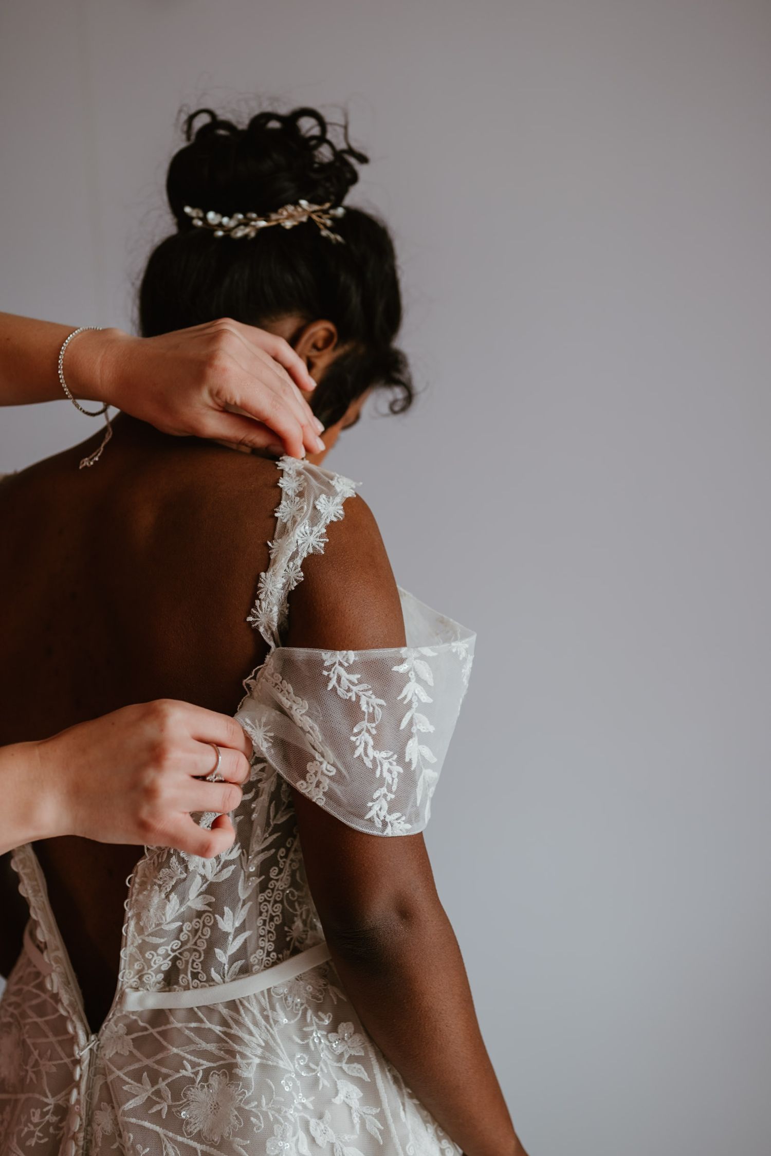 Close-up detail of a delicate lace wedding dress being fastened, showing intricate floral embroidery patterns.