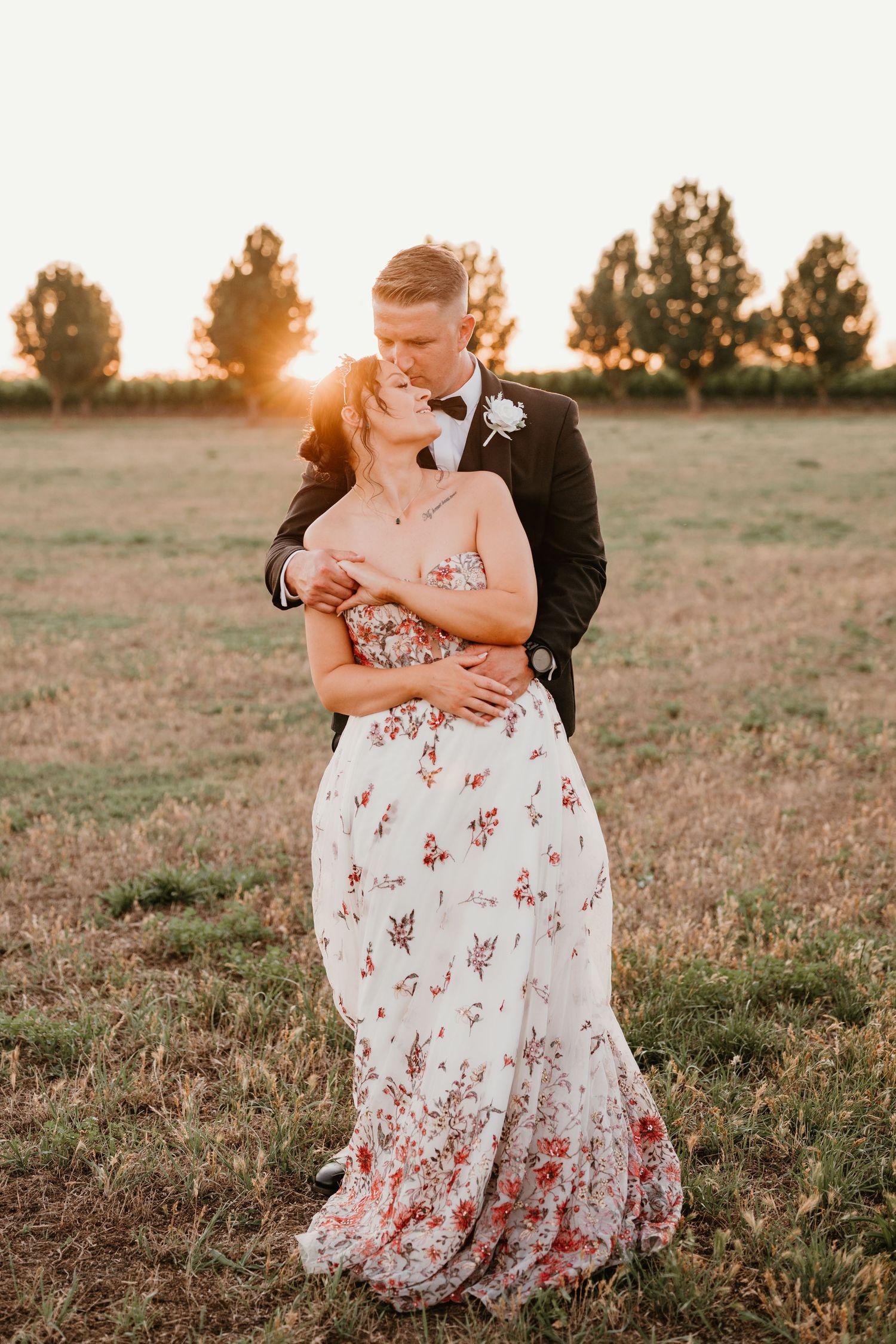 A romantic sunset wedding photo featuring a couple embracing in a field with a floral wedding dress.