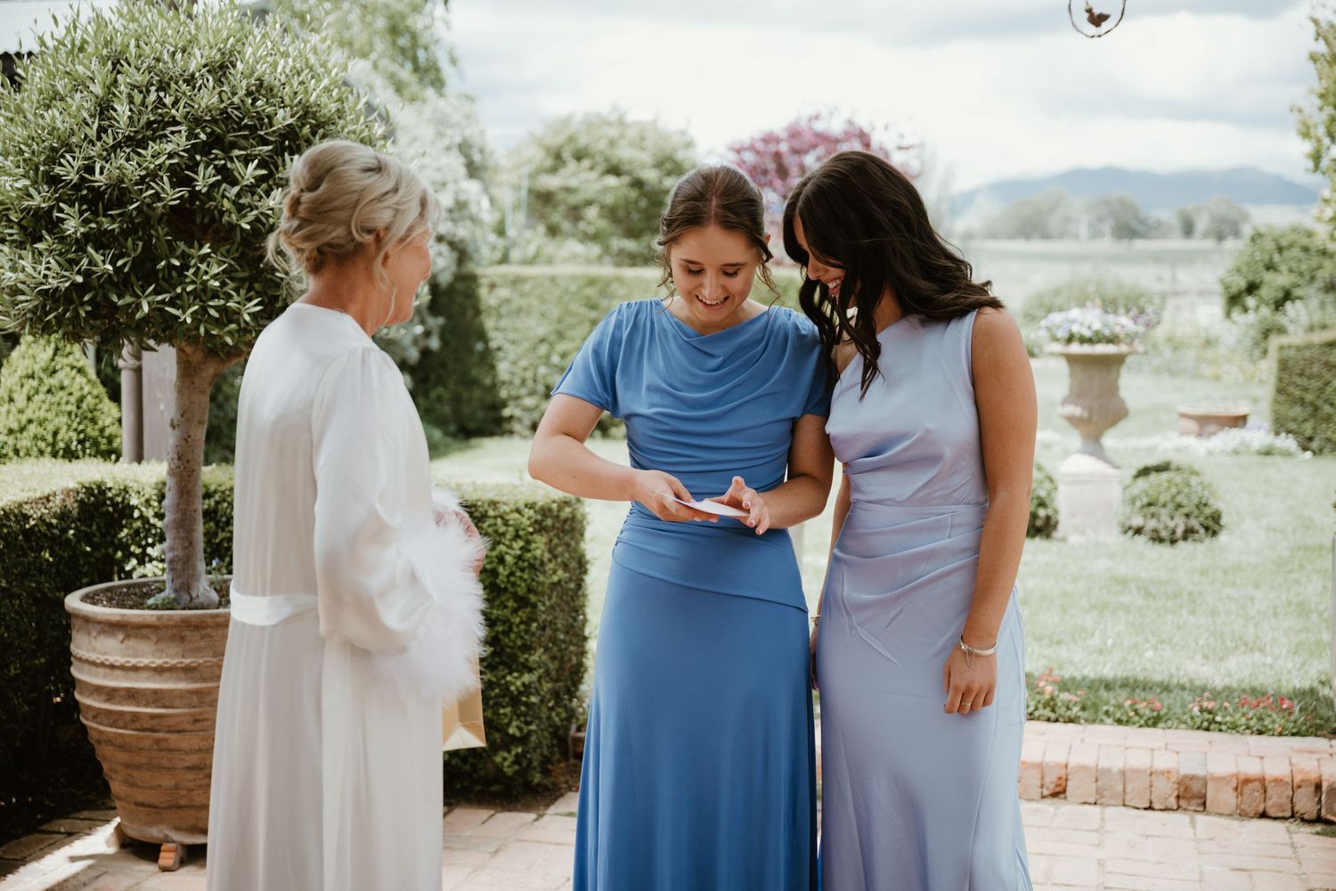 A group in coordinating blue and white outfits shares emotional moments together in an outdoor garden setting.