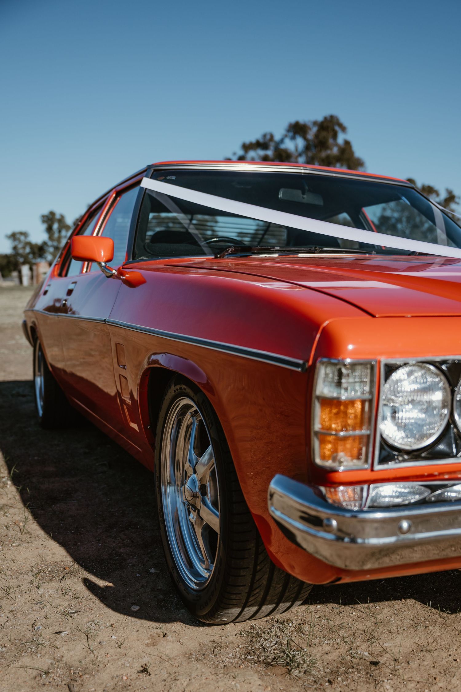 A vintage orange muscle car with custom chrome wheels photographed at a low angle.