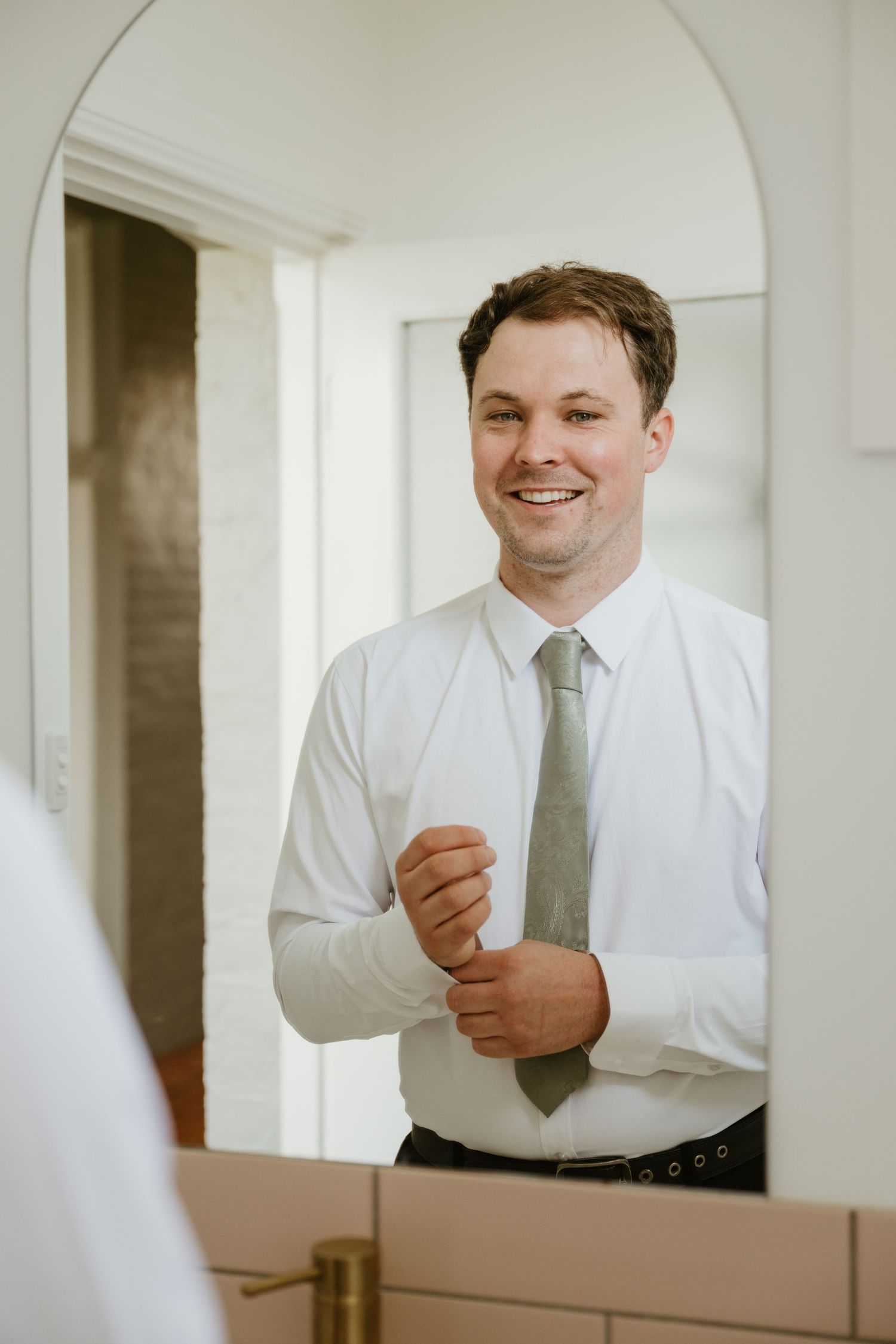 A person in a white dress shirt and tie adjusts their cuffs while getting ready.