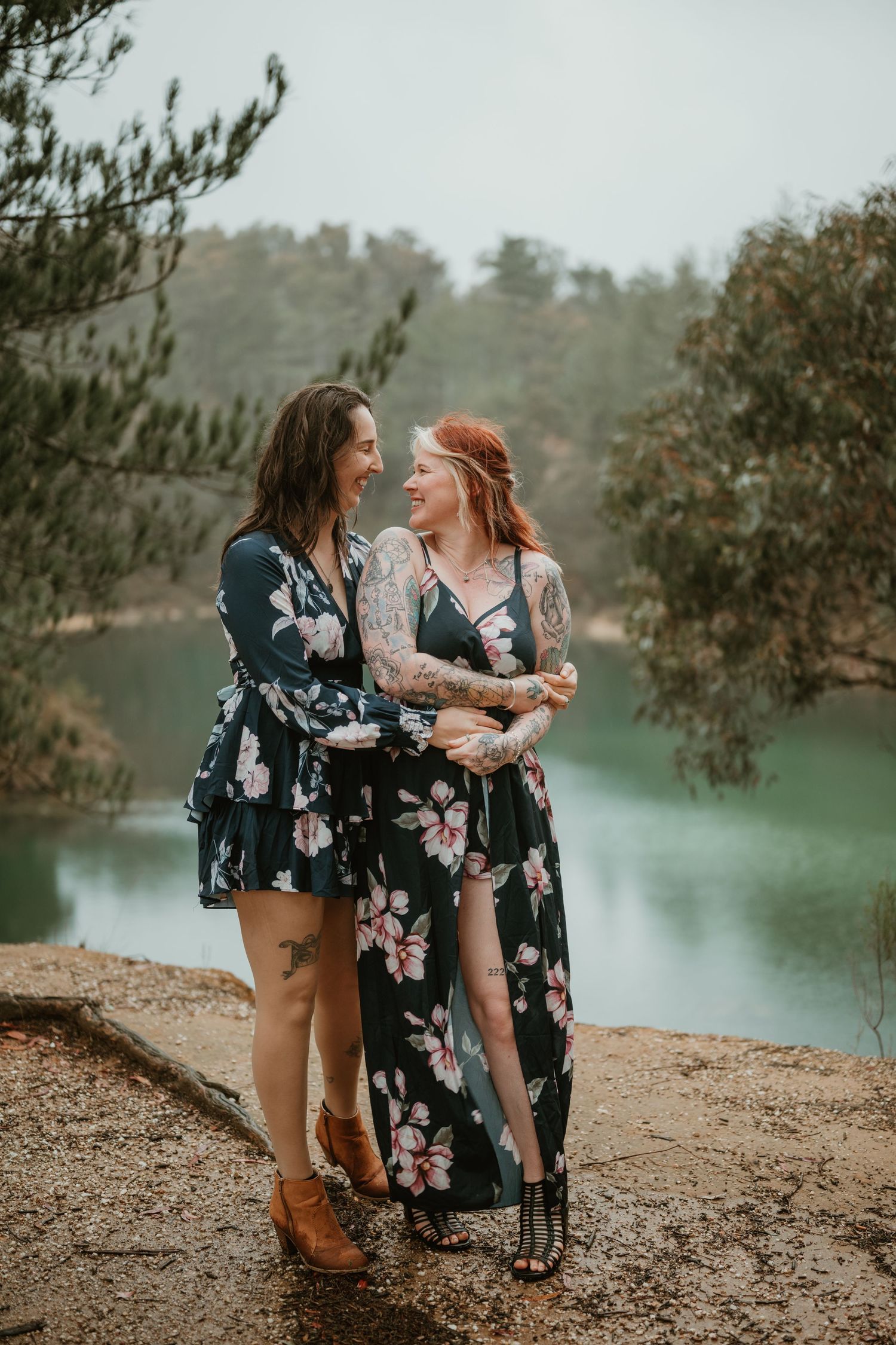 Couple in matching floral dresses share a tender moment by serene lake.