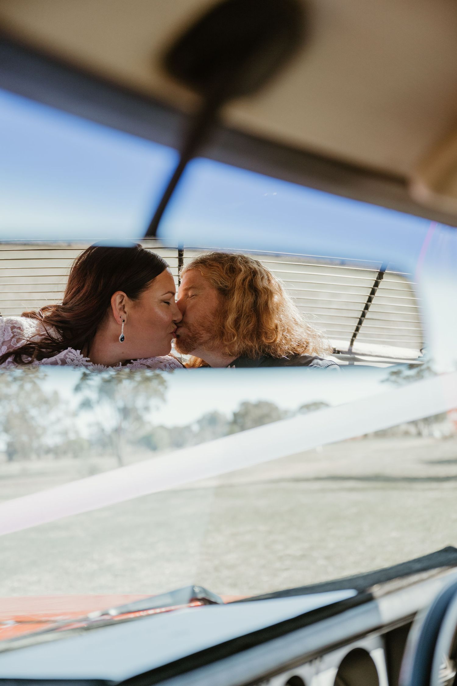 Two people share a romantic kiss viewed through the windshield of a car.