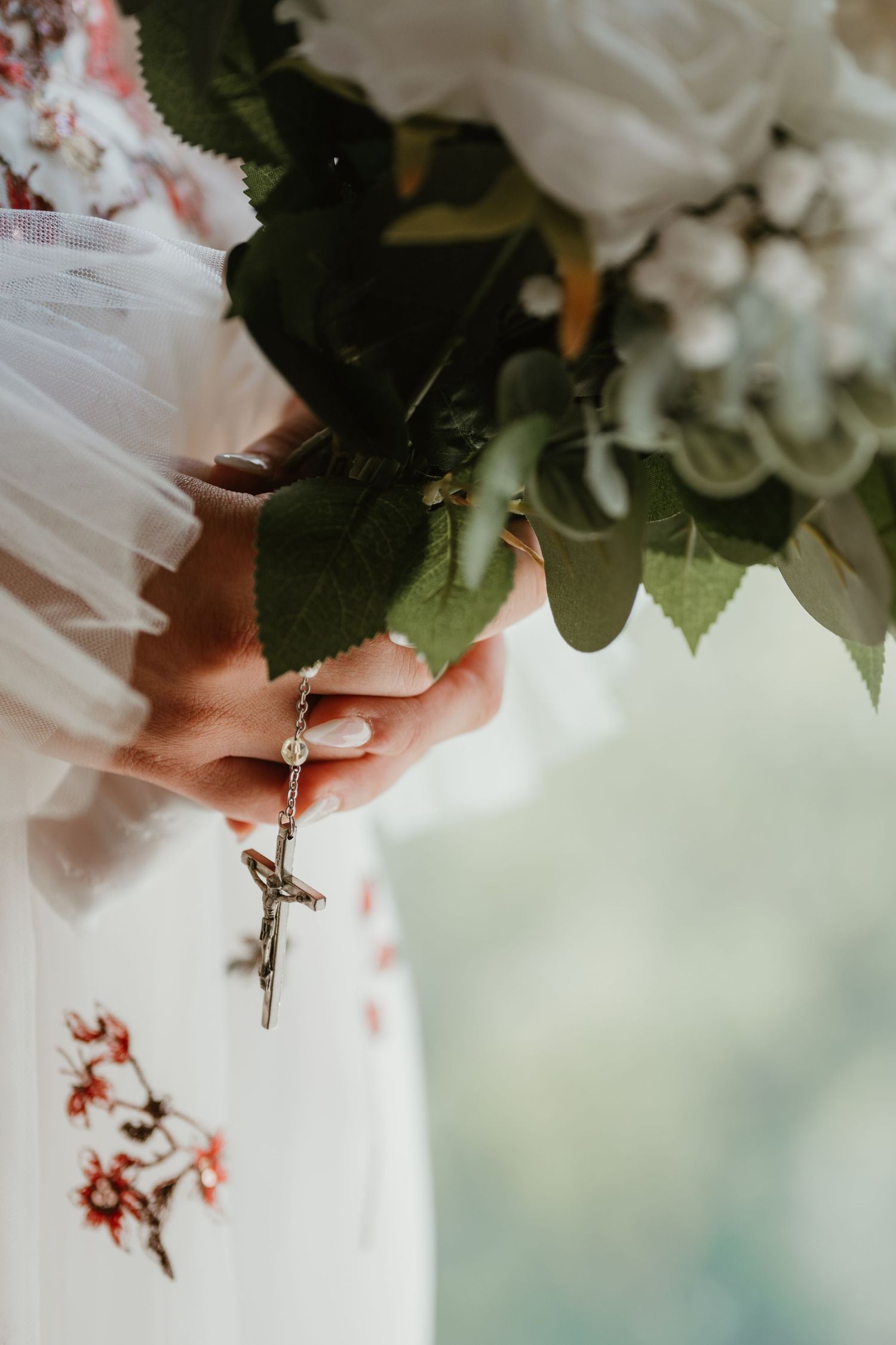 Close-up of hands holding a wedding bouquet with a delicate cross pendant.