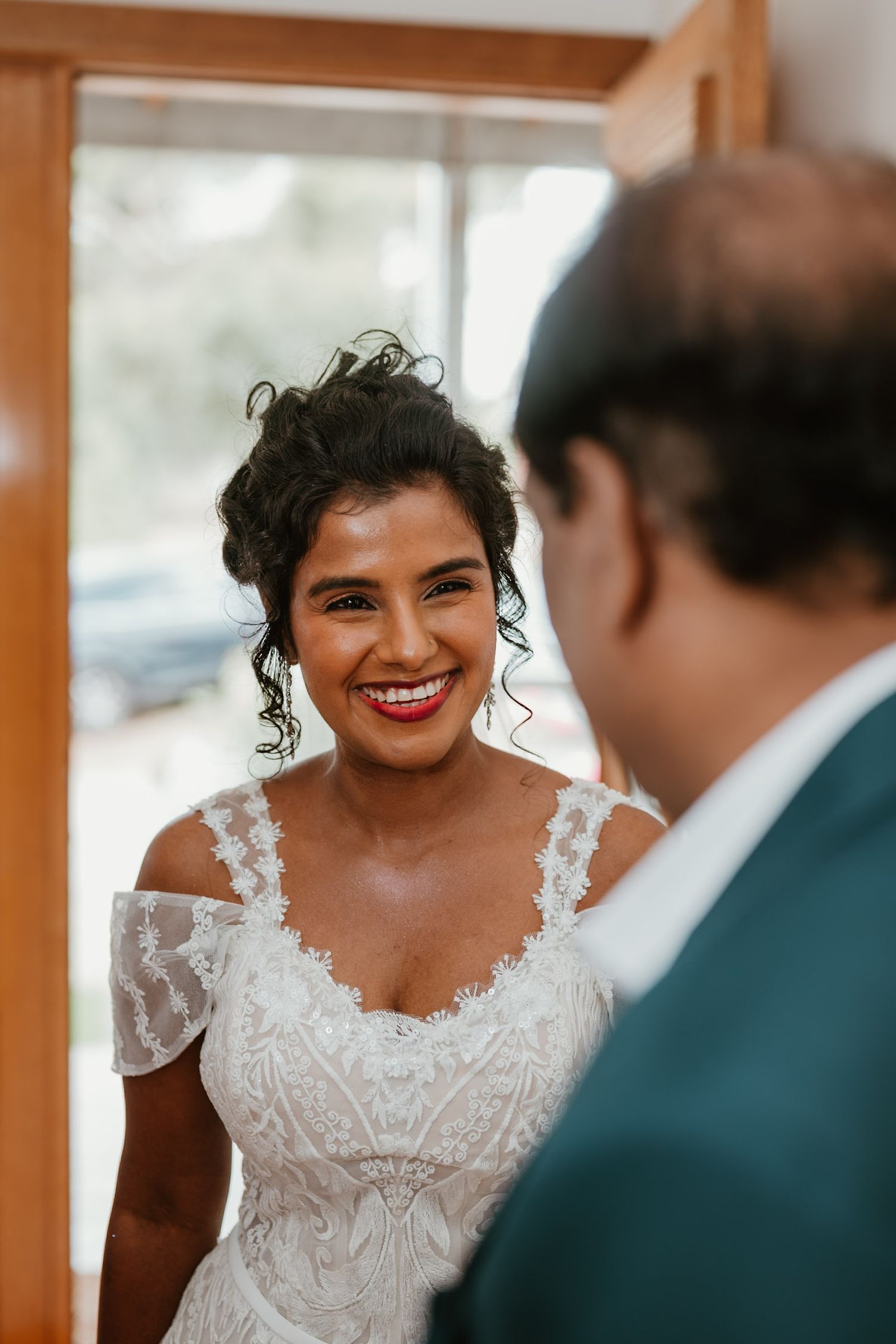 A radiant bride wearing an ornate lace wedding dress with delicate straps.