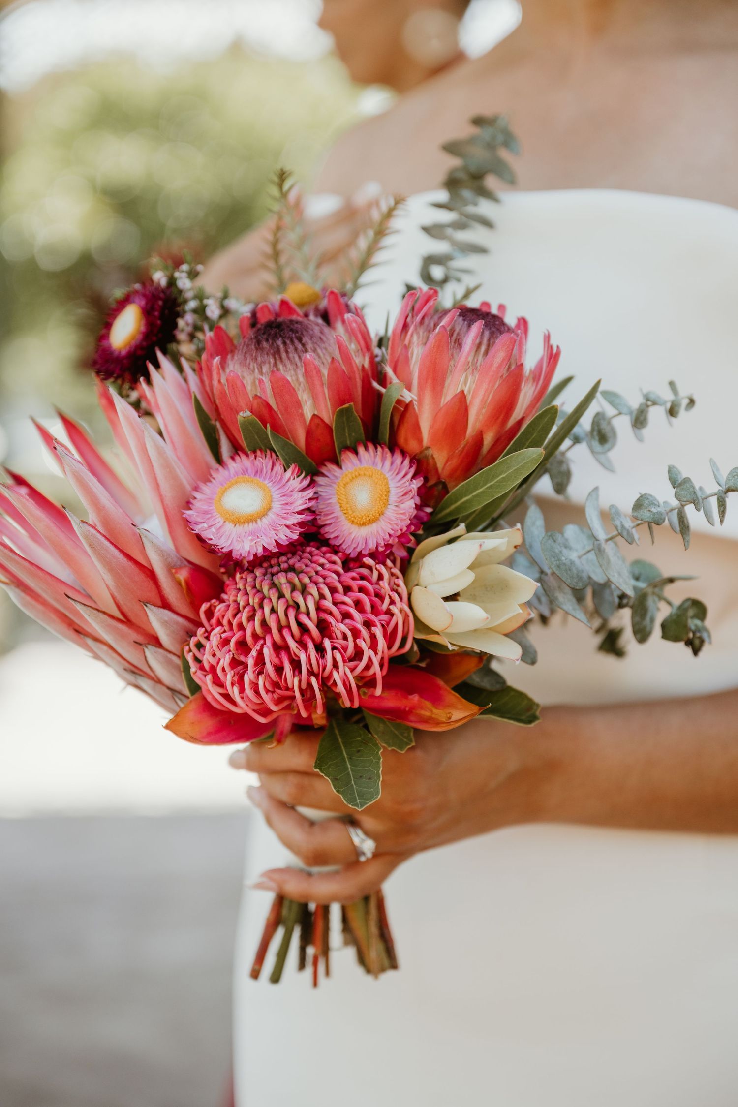Close-up view of pink and coral protea flowers with eucalyptus leaves arranged in a modern floral centerpiece.