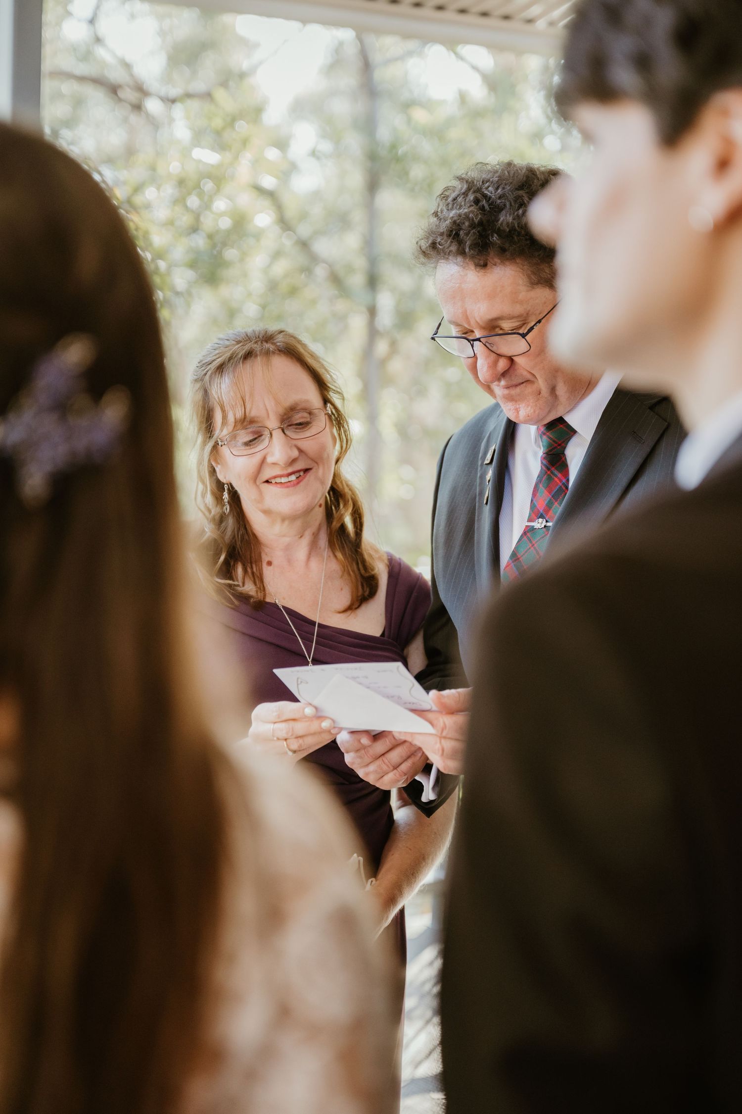 Wedding guests gather outdoors reading ceremony programs in natural lighting.