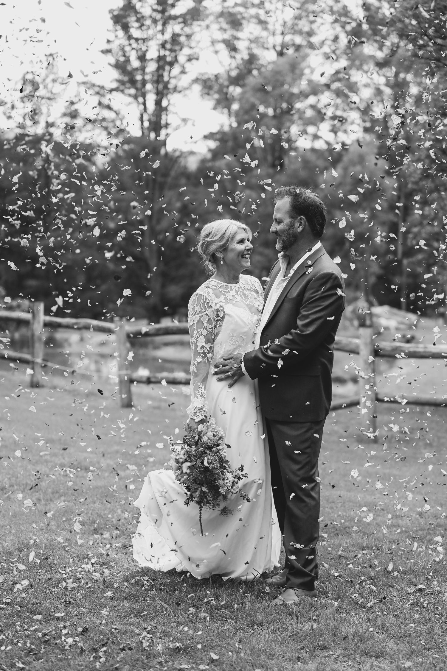 A romantic black and white wedding photo sequence showing a couple embracing as flower petals fall around them in a garden.