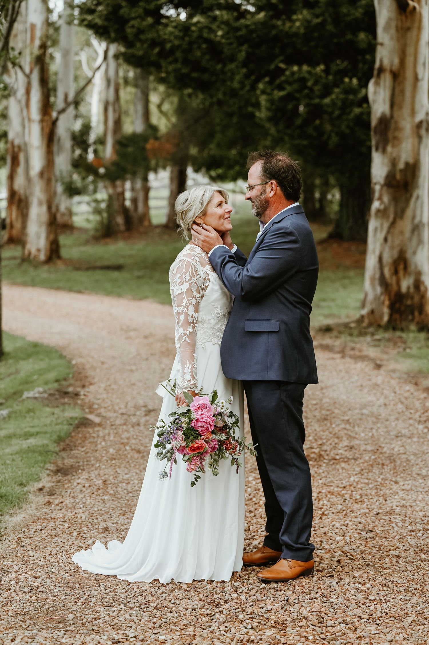 Newlywed couple shares intimate moments along a tree-lined path covered in autumn leaves during their wedding photoshoot.