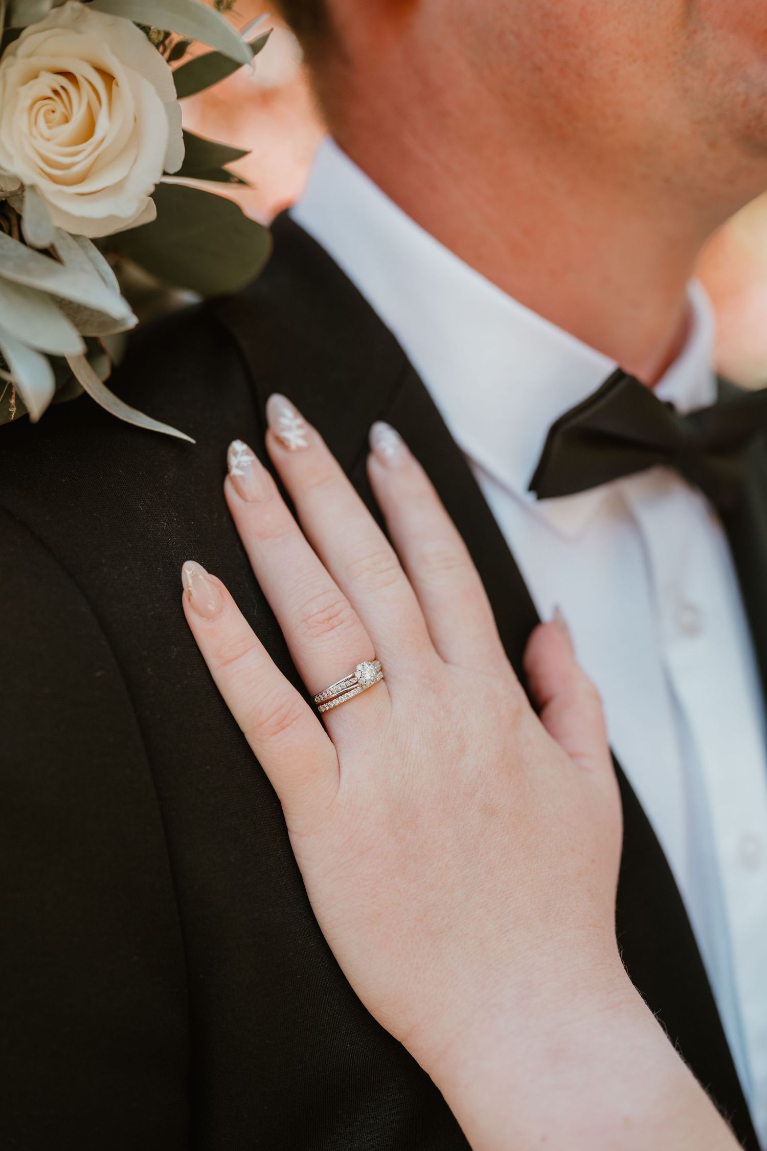 Close-up detail of a diamond wedding ring on a hand against formal attire.