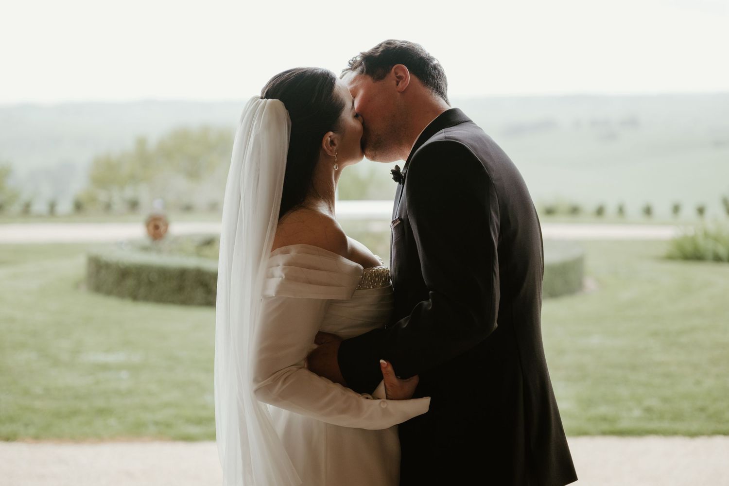 A couple embraces outdoors in a romantic moment against a misty natural landscape backdrop.