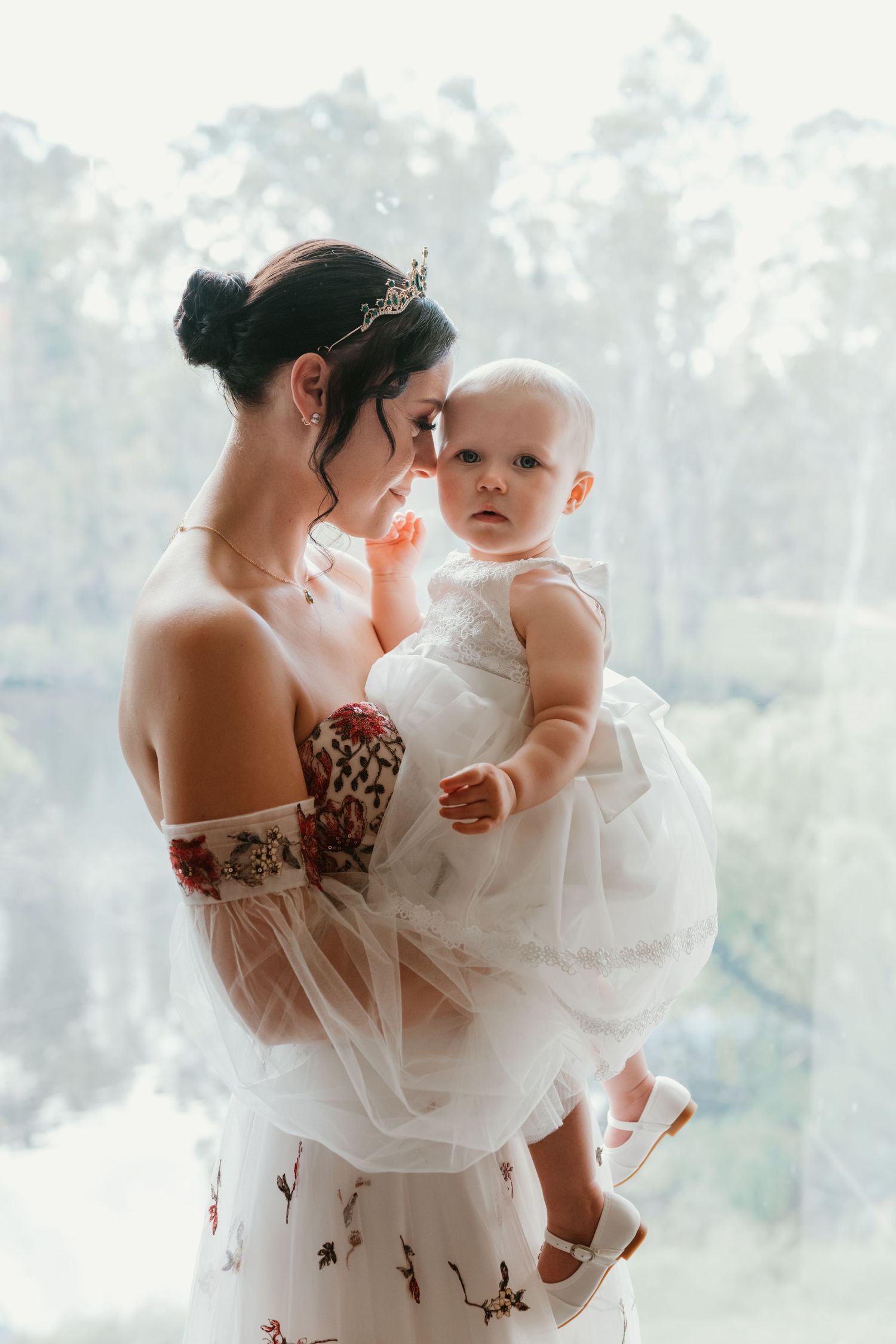 Sweet moment with baby in white dress during wedding preparations.