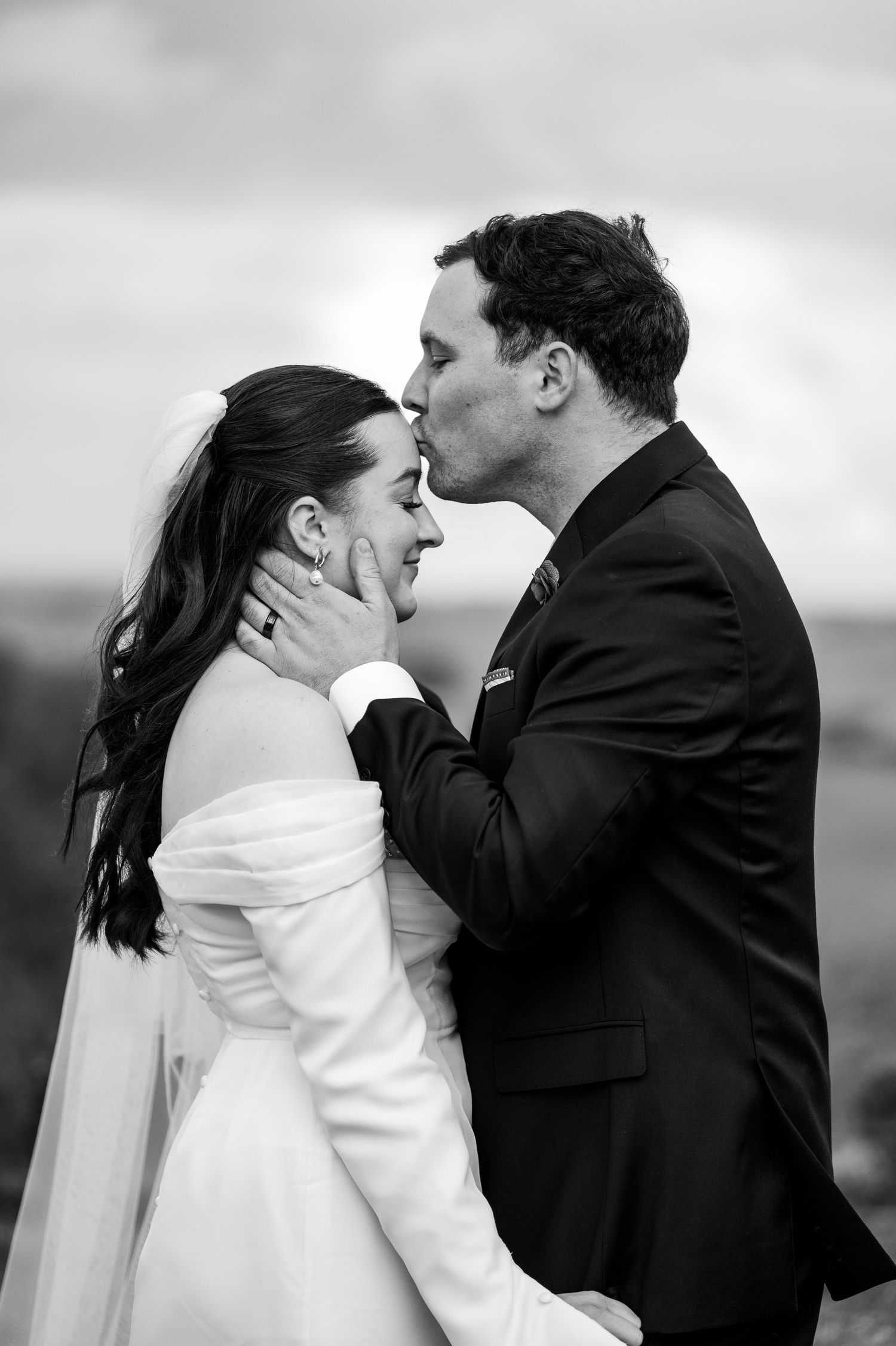 A tender black and white wedding moment captured as a couple shares an intimate kiss outdoors.