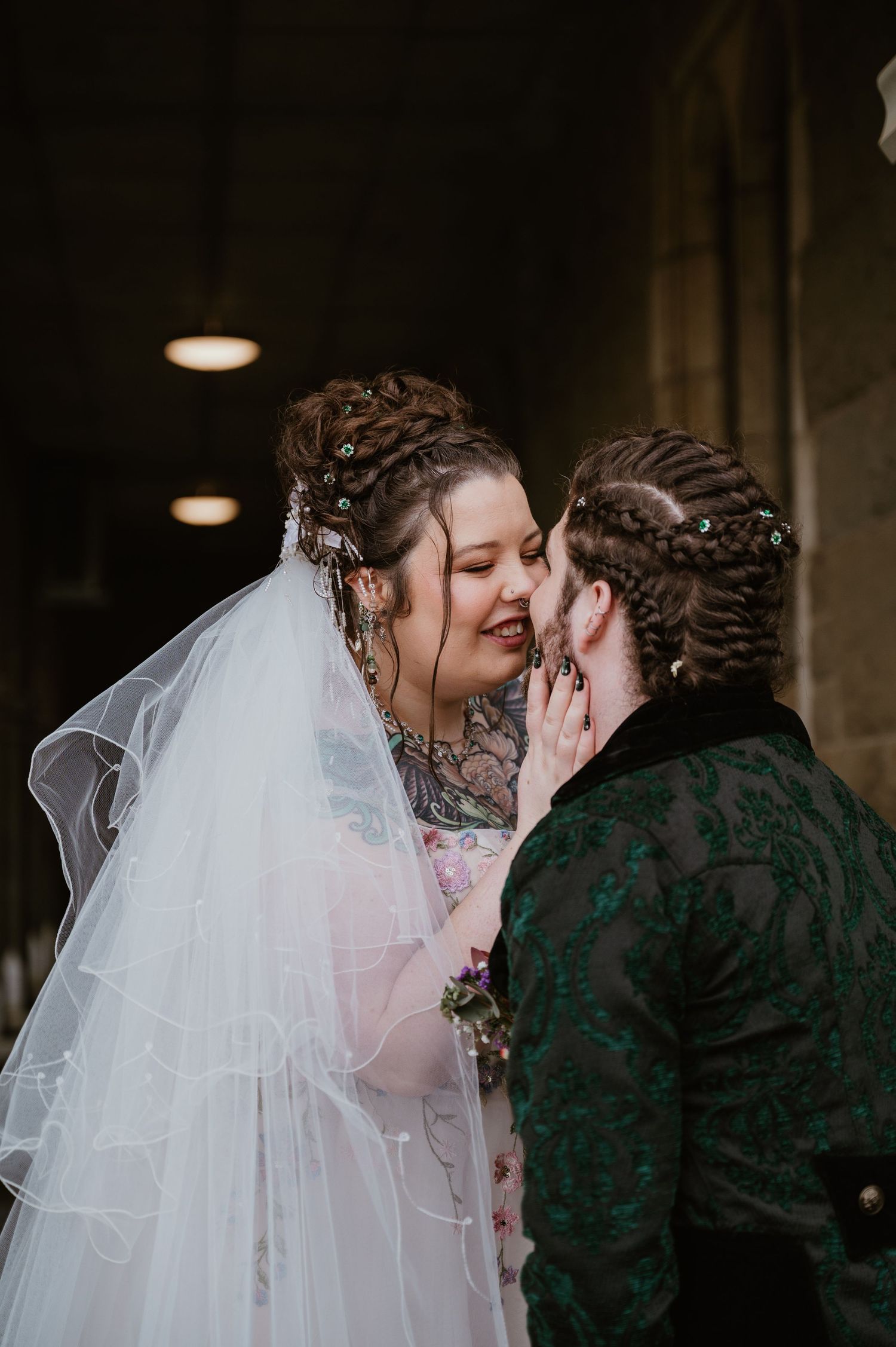 A tender wedding moment between two people in ornate attire, with the bride wearing a flowing white veil.