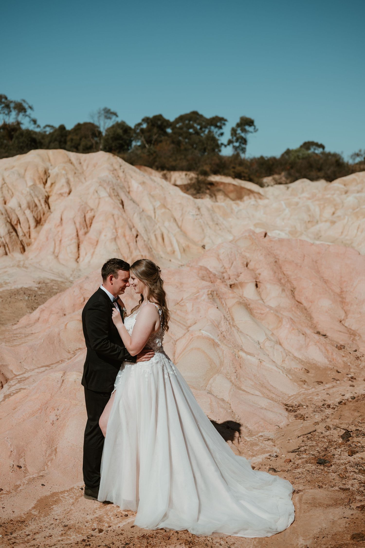 Wedding couple embracing against pink desert rock formations during sunset.