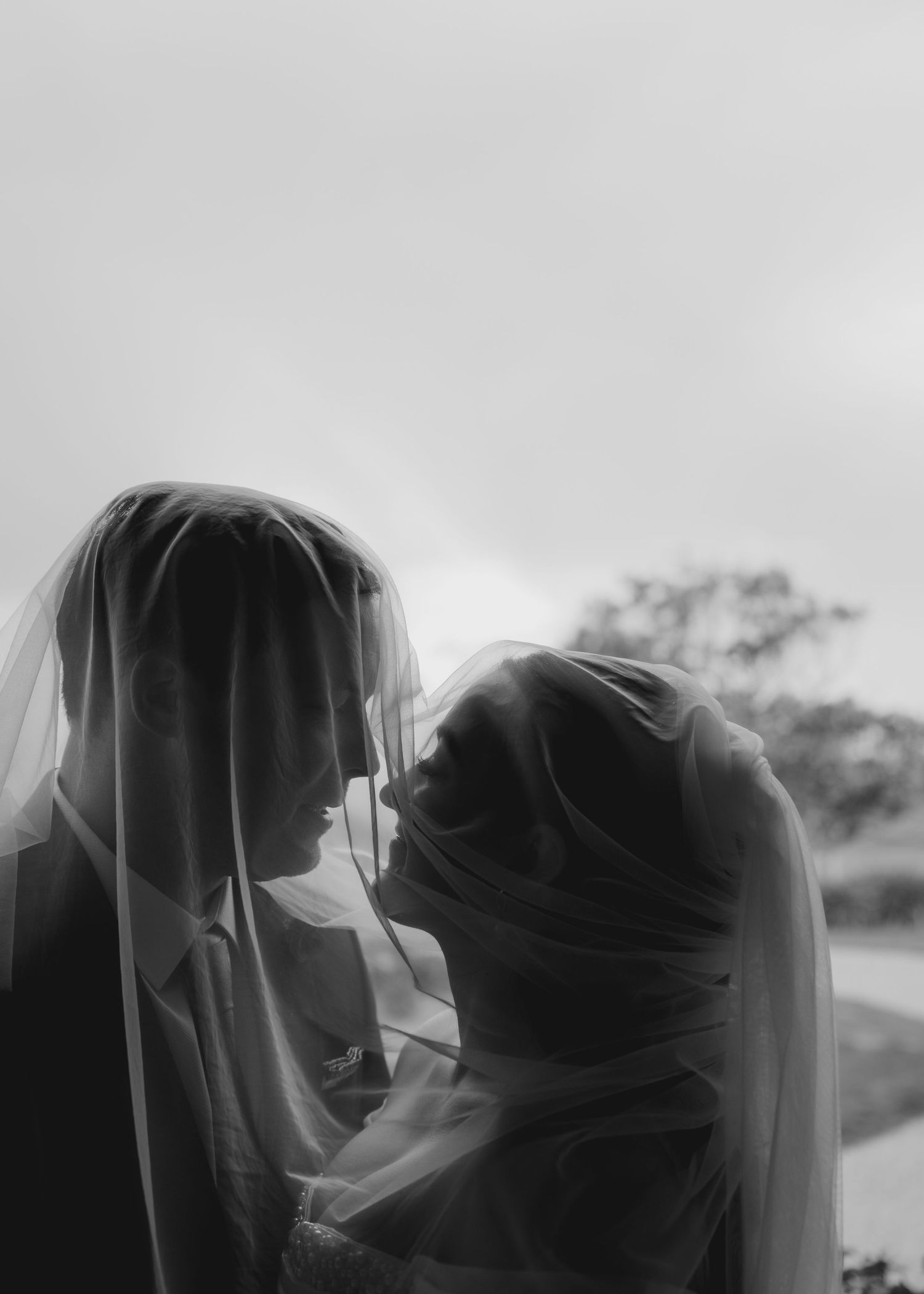 A black and white photograph shows a couple in silhouette sharing a romantic kiss outdoors.