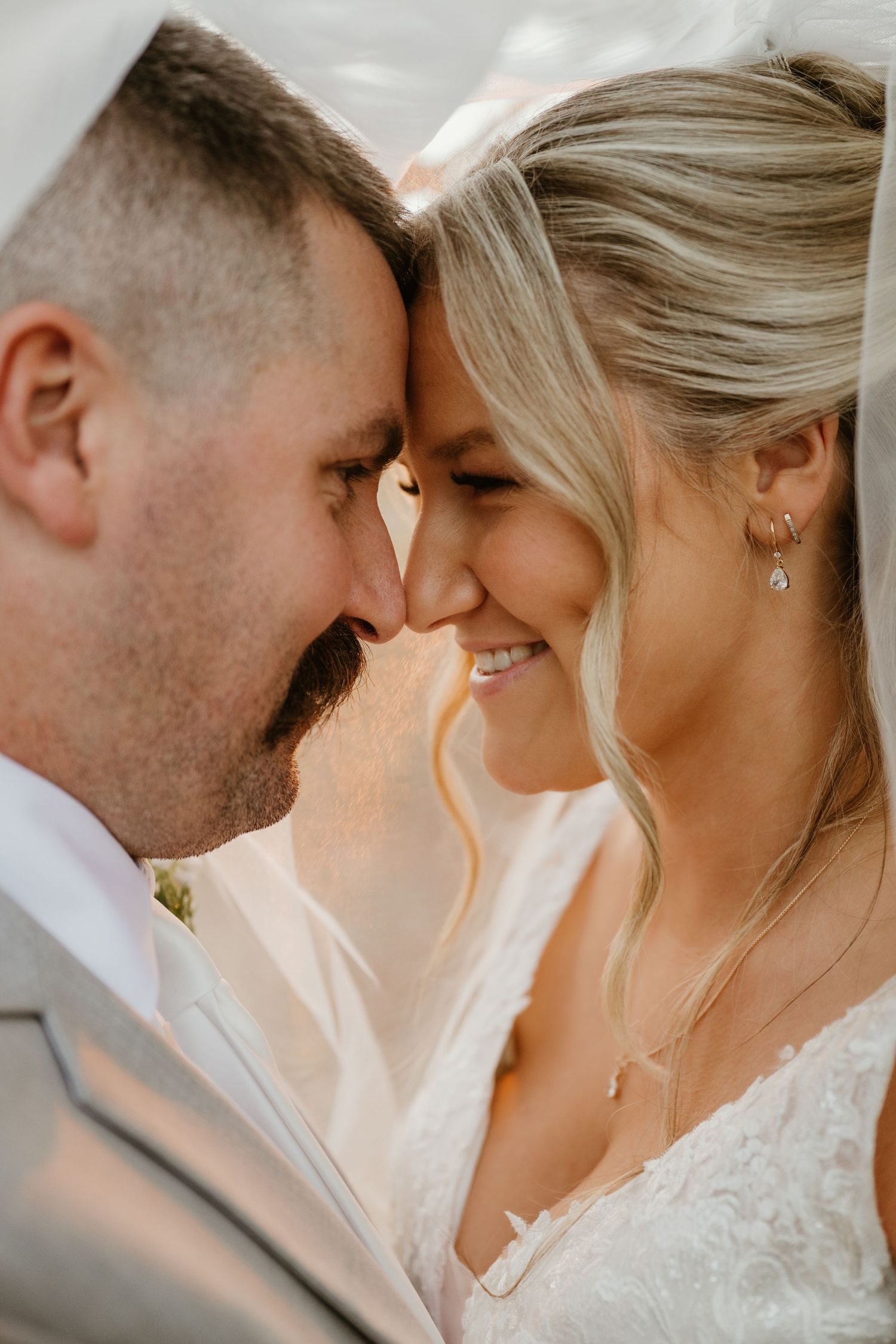 A bride and groom touch foreheads and smile tenderly in a romantic close-up wedding portrait.