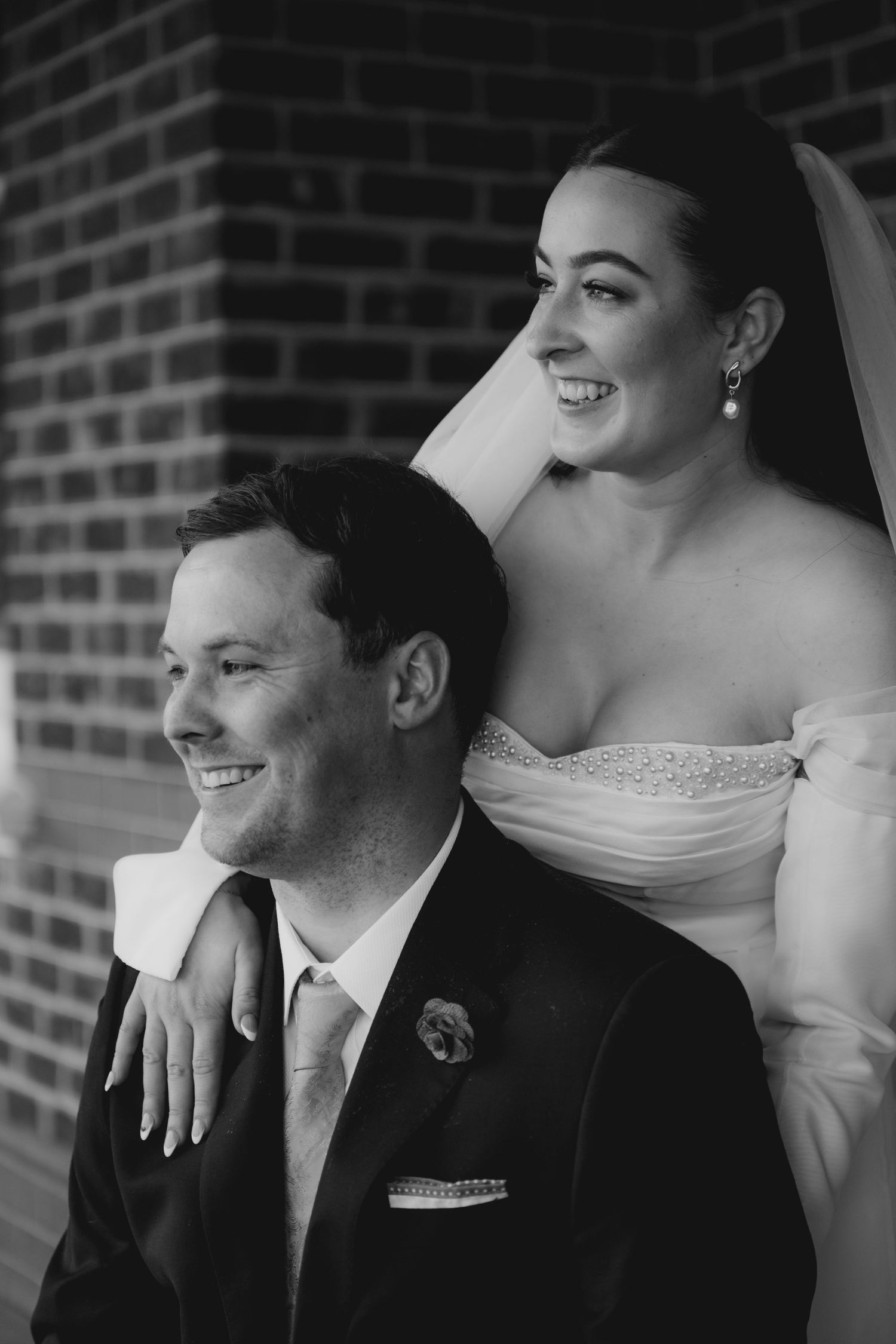 Black and white wedding photo series showing romantic candid moments between newlyweds against a brick wall.