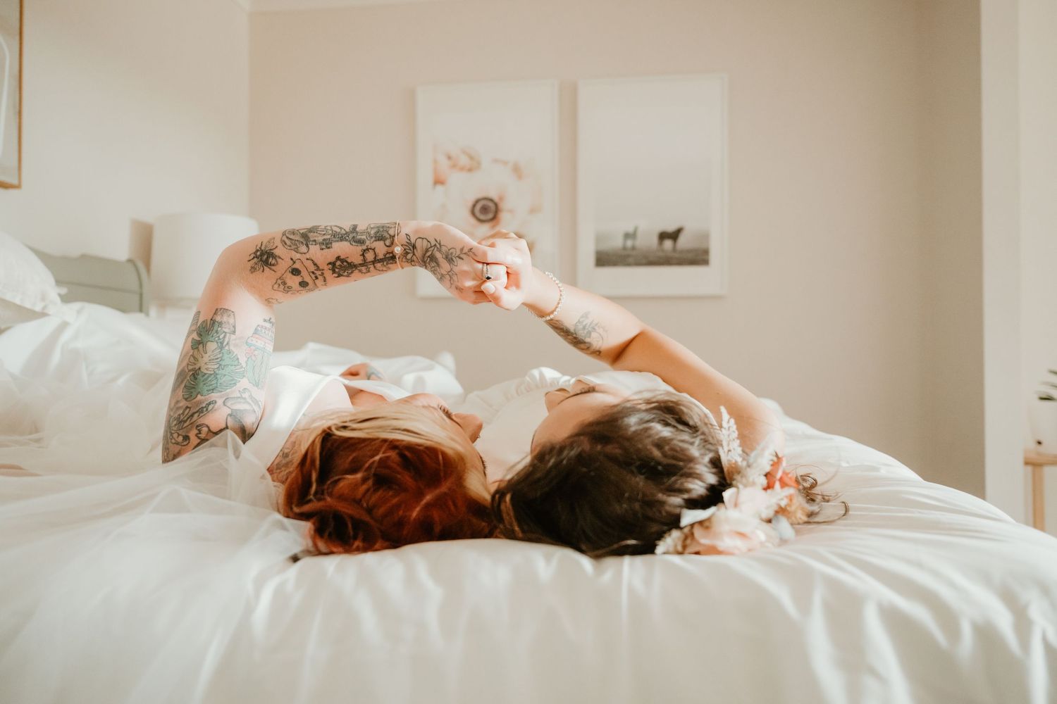 Intimate moment between couple in white dresses captured on white bedding.