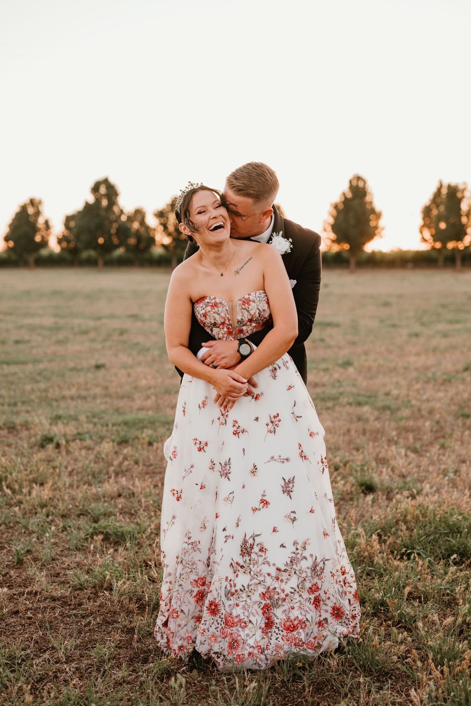 Joyful wedding couple laughing together in a field at sunset.