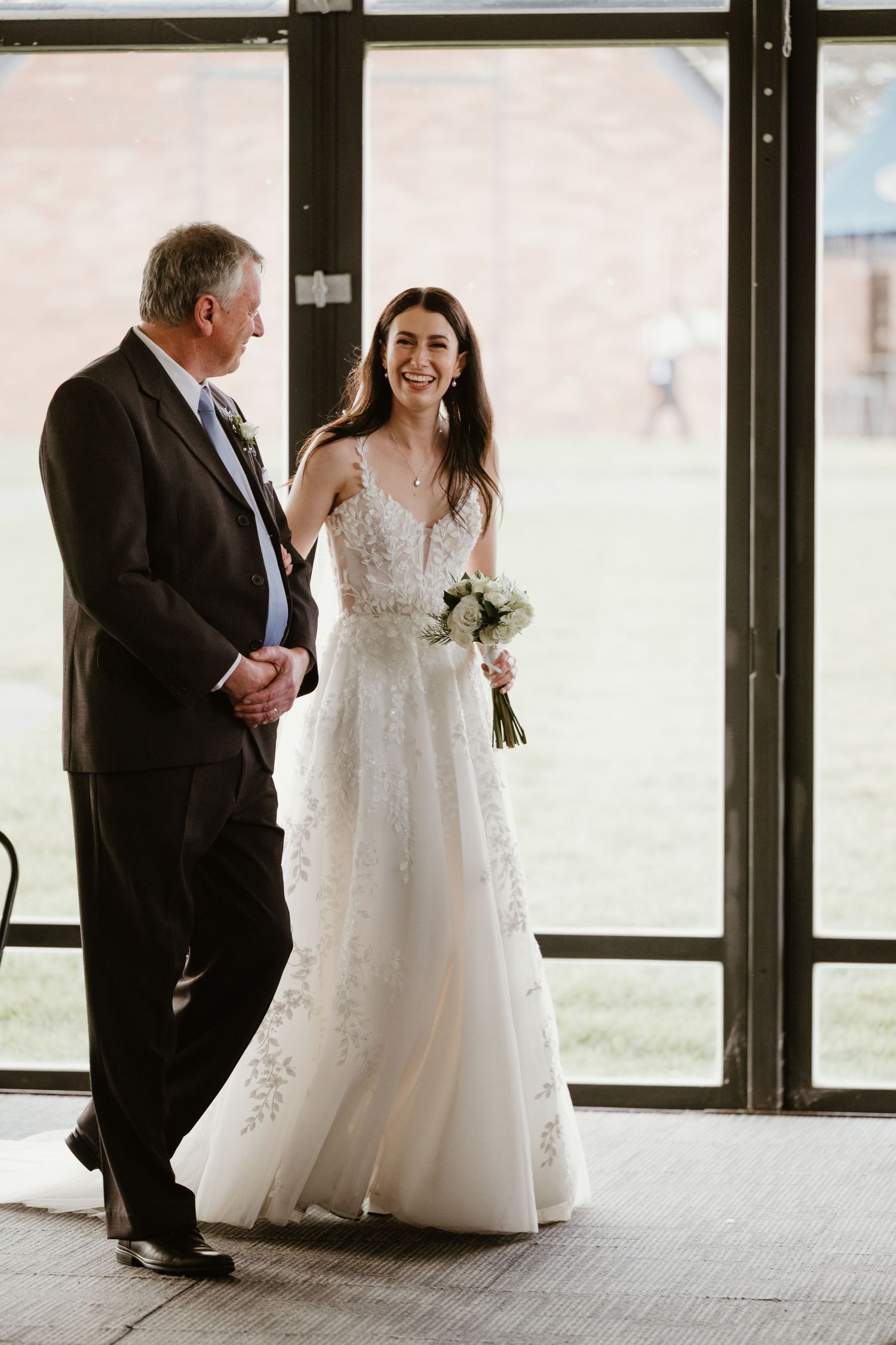 A wedding couple sharing a joyful moment in front of glass windows.