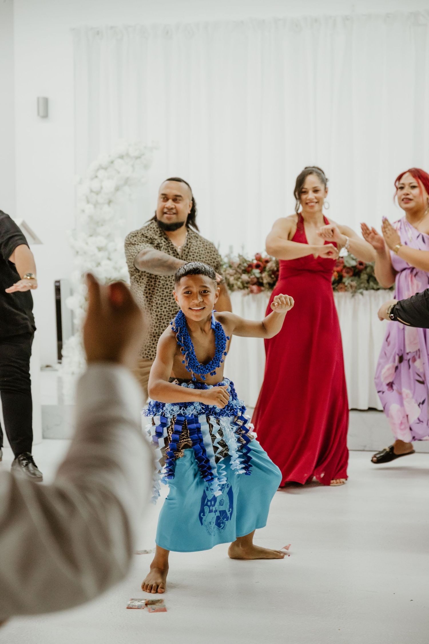 People dancing and celebrating at a wedding reception with traditional Pacific Islander attire and decorations.