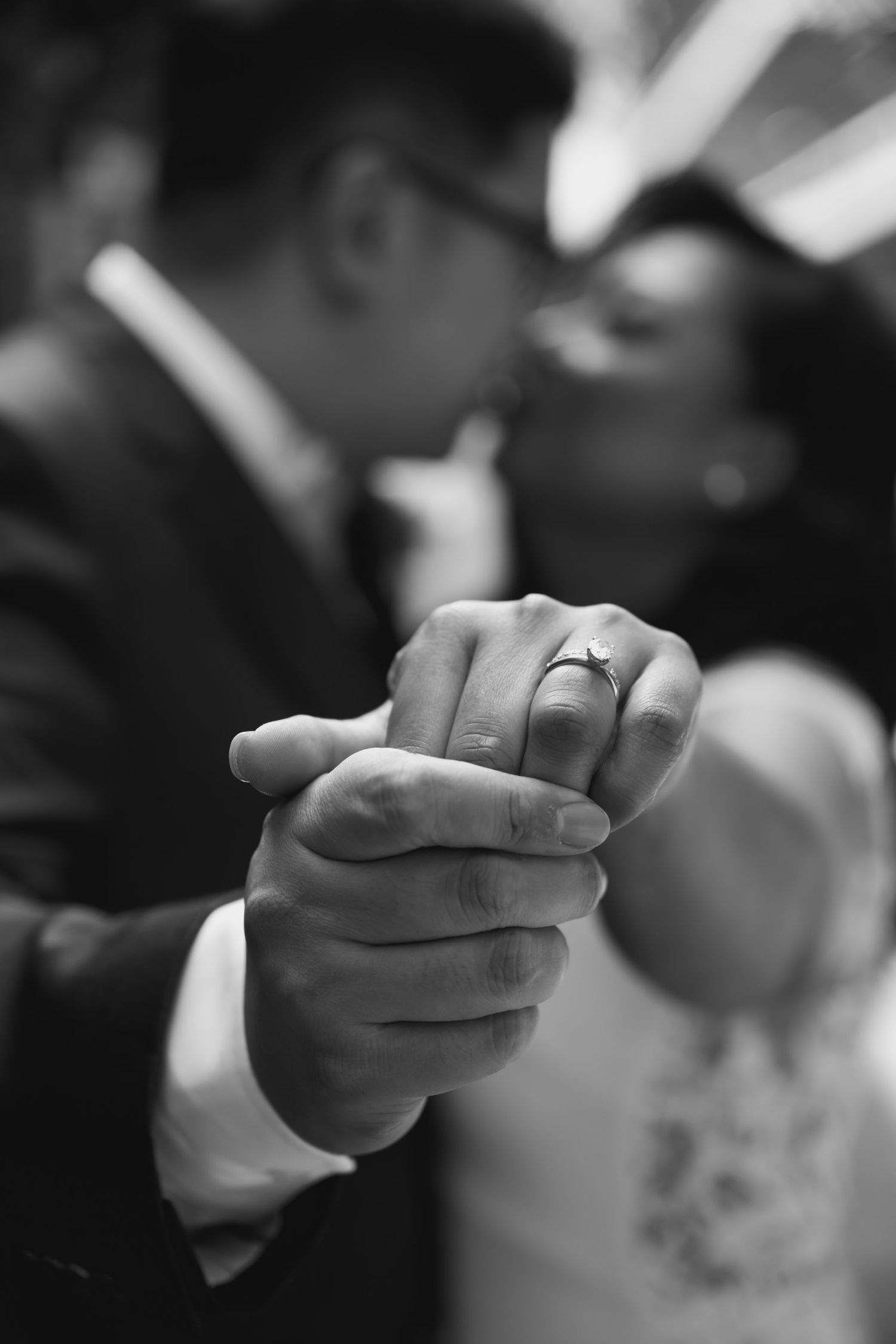 Black and white macro photo series showing hands holding and exchanging a wedding ring during a ceremony.