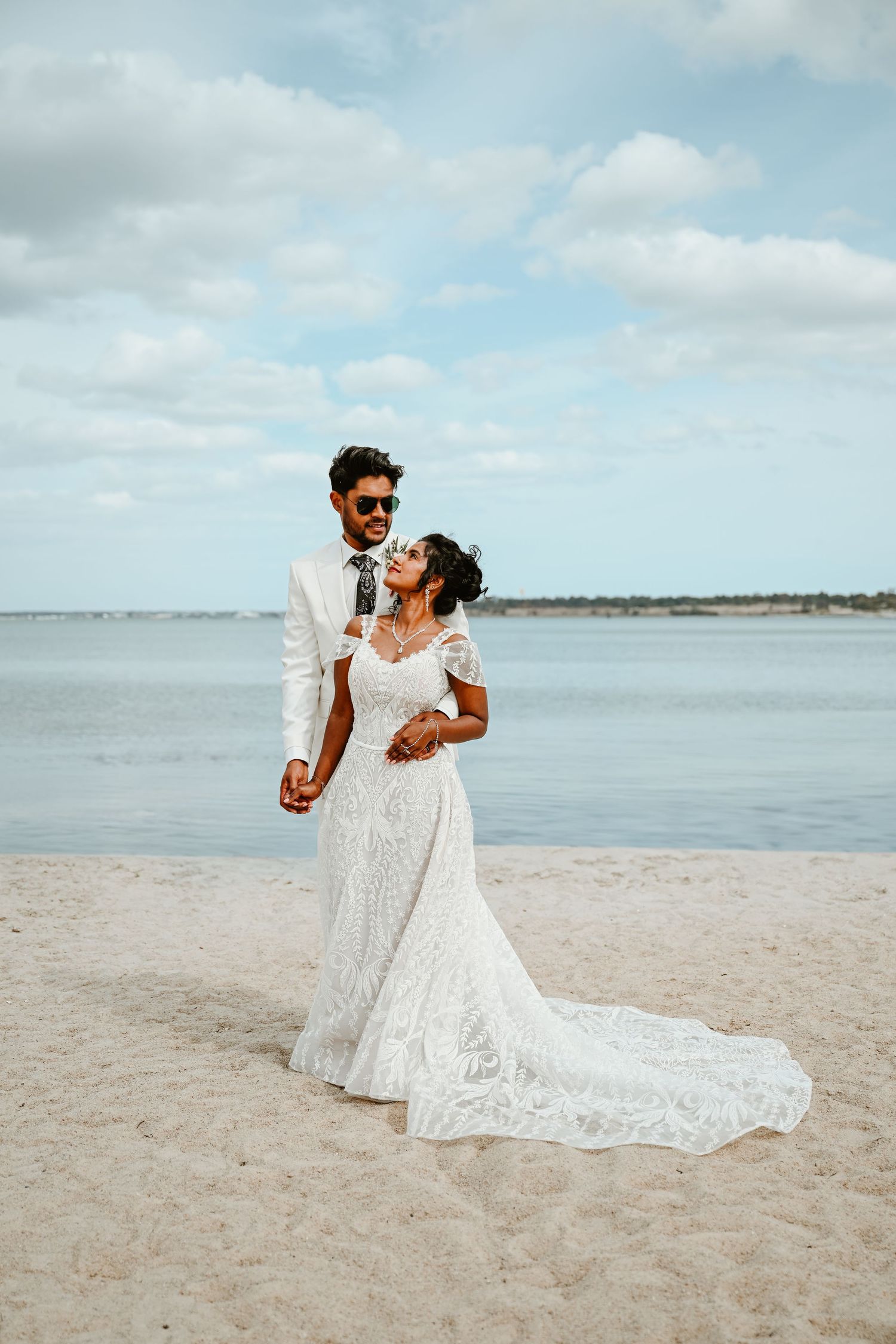 A romantic beachside wedding photoshoot features a couple in white attire against the ocean backdrop.