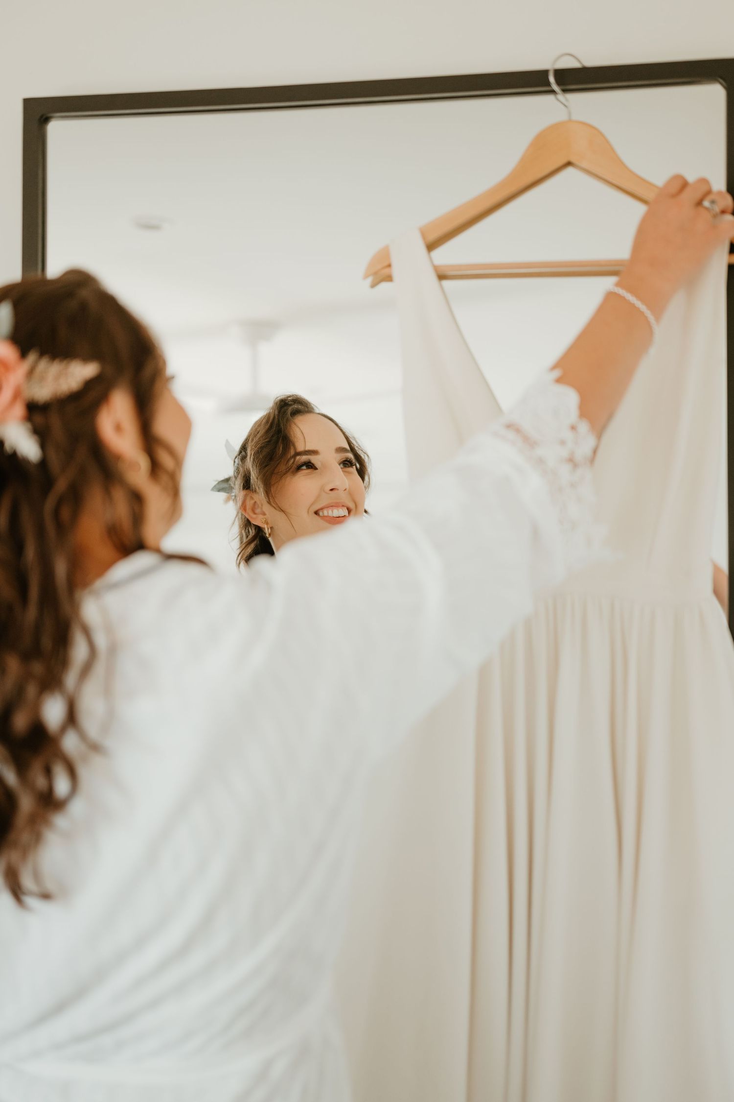 White wedding dresses hanging on hangers against a light colored wall.